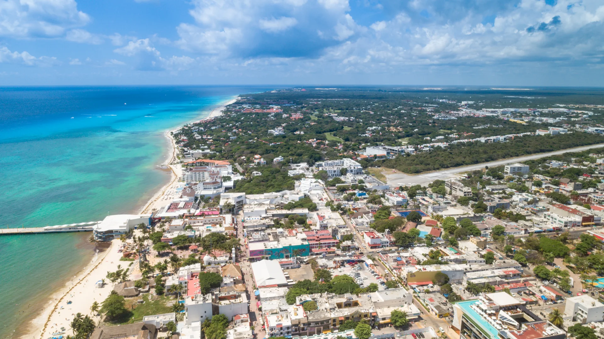 Vista aérea diurna de Playa del Carmen, com o centro urbano, a faixa de praia e o mar do Caribe.