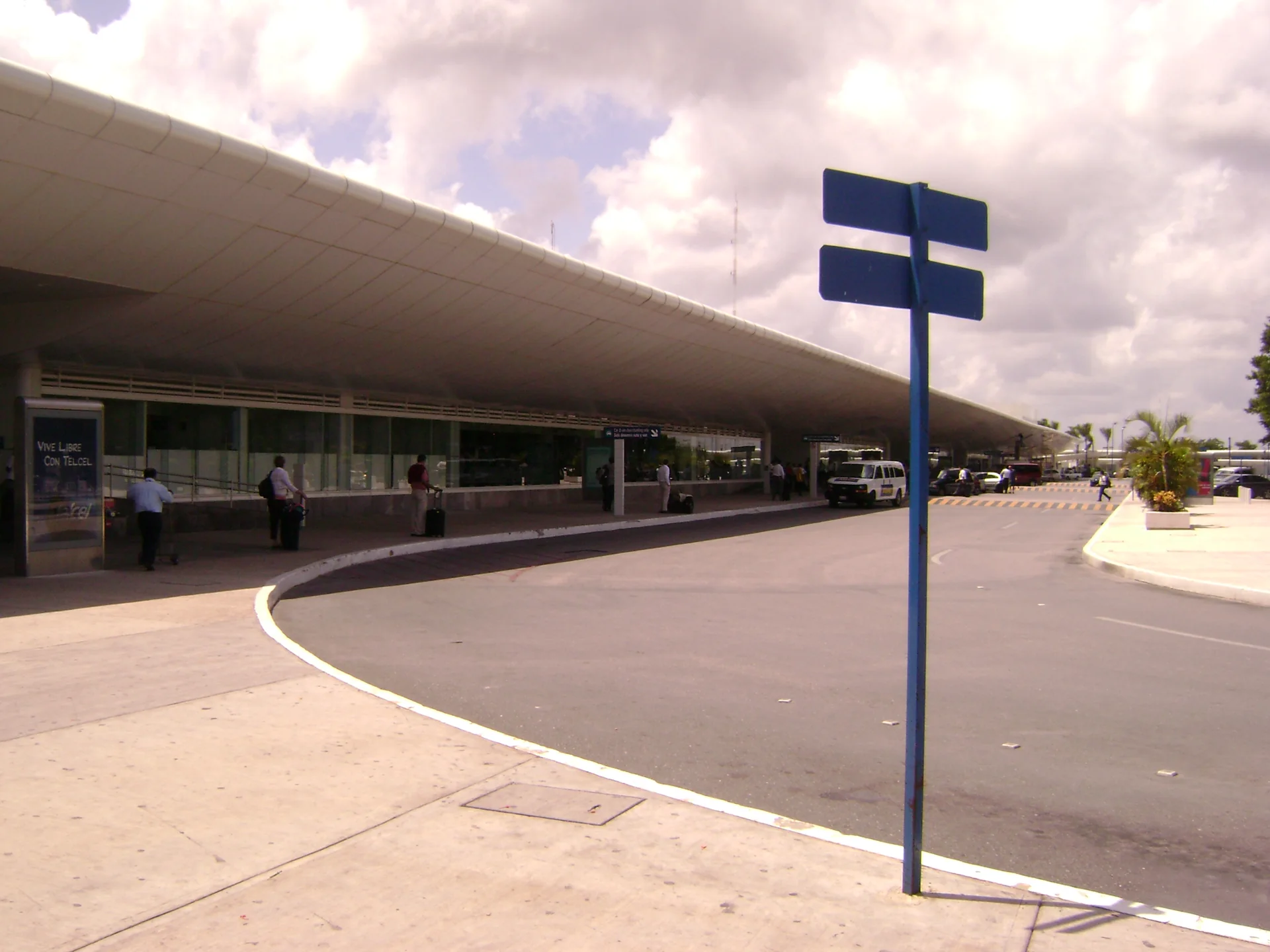 Área externa do Aeroporto Internacional de Cancún, vista durante o dia, com calçada e acesso viário do terminal.
