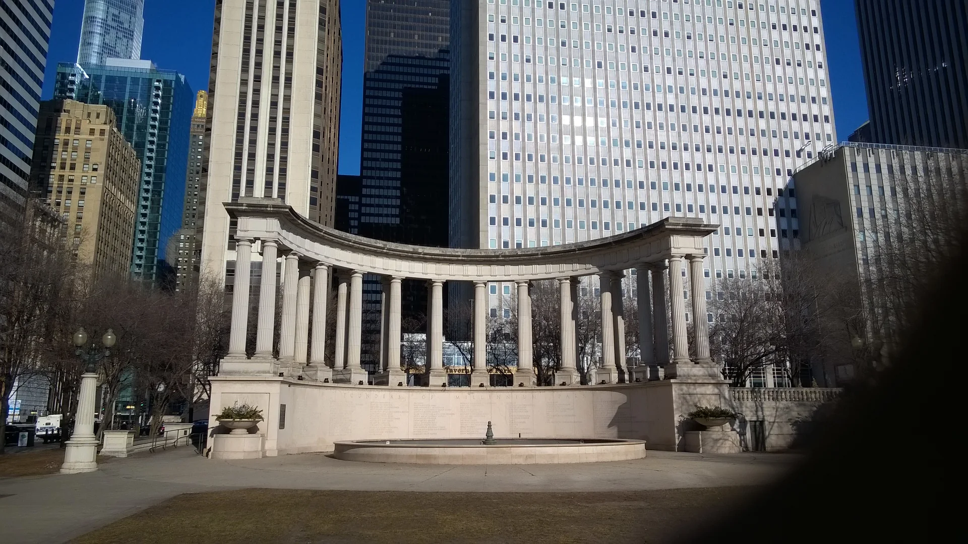 Colunata de pedra de Millennium Park diante de prédios altos do centro de Chicago em um dia ensolarado.