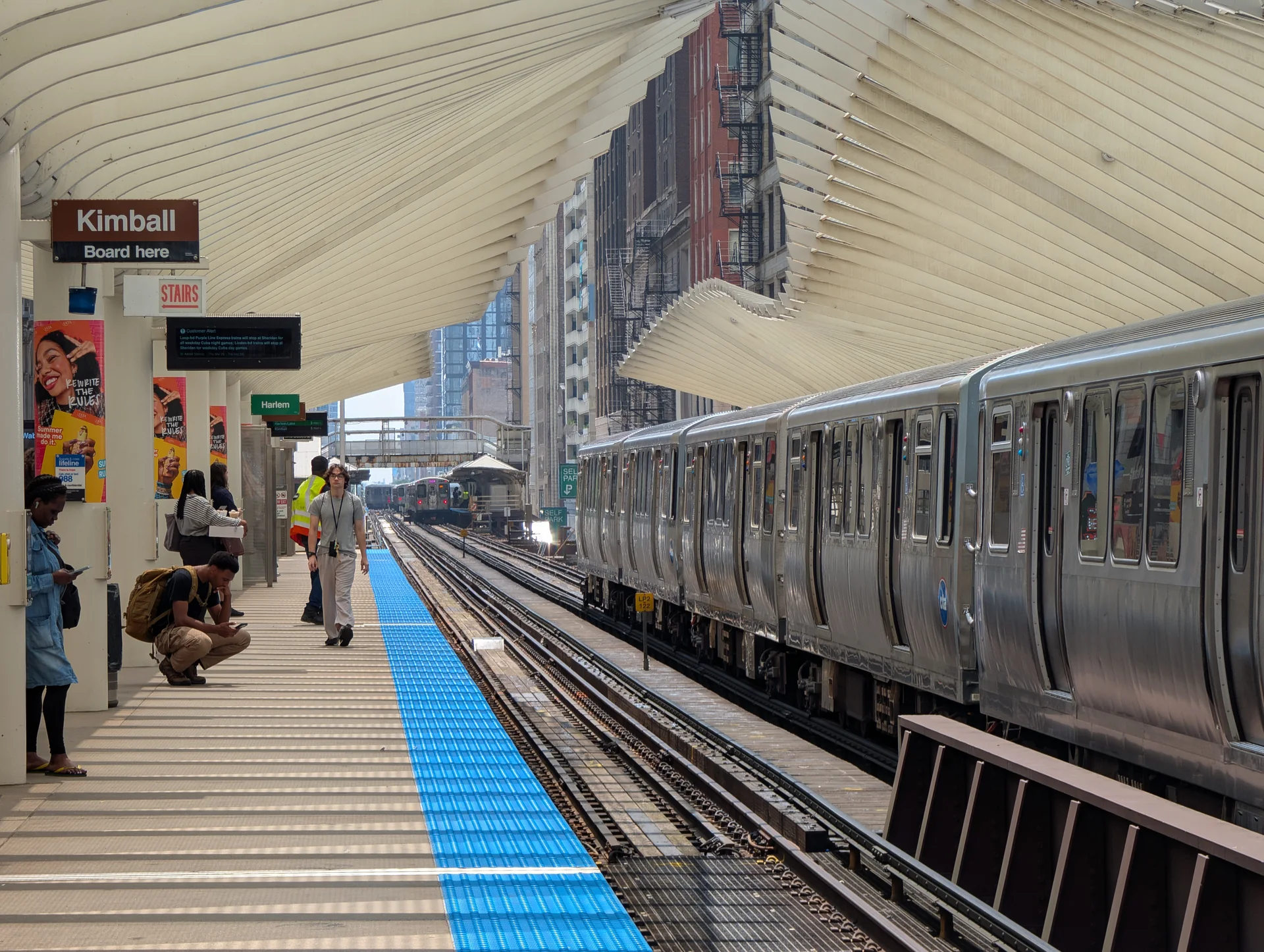 Trem prateado da CTA parado na plataforma elevada Washington/Wabash, no Loop, com passageiros e trilhos seguindo entre os edifícios.