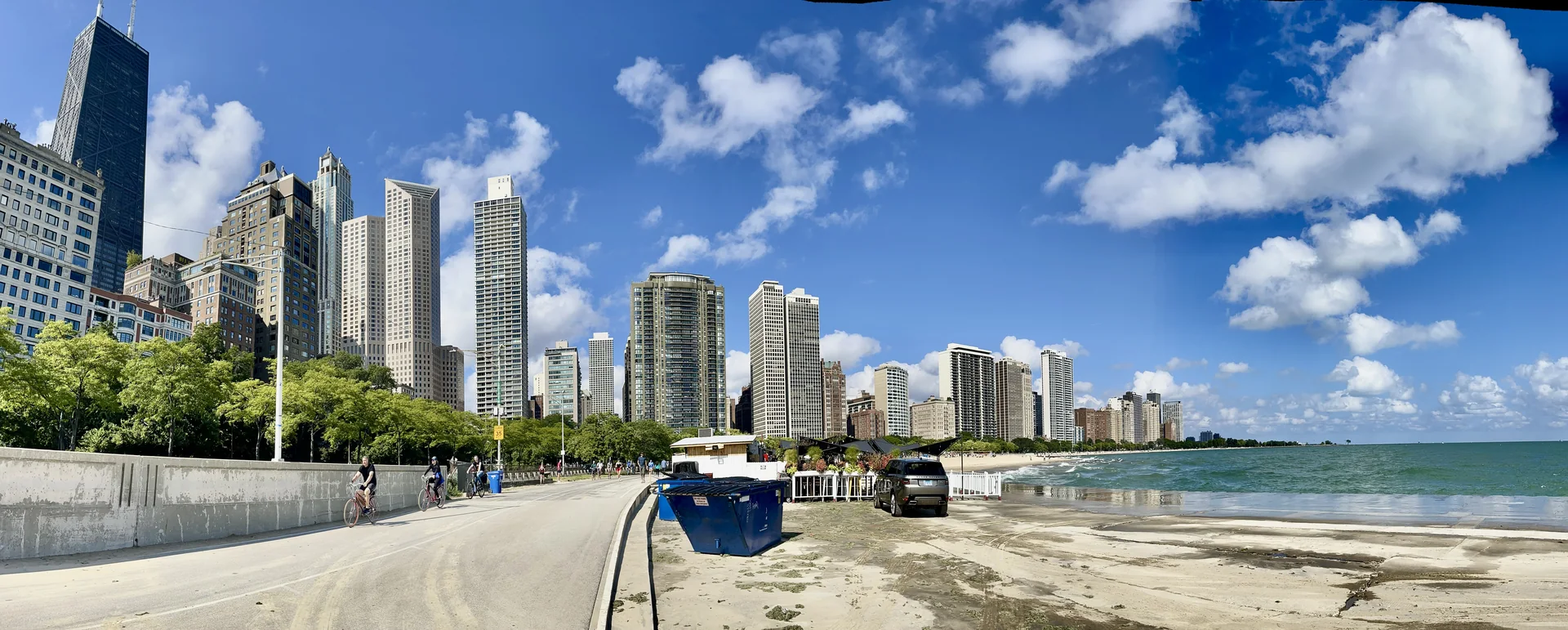 Ciclistas percorrem o Lakefront Trail em manhã clara, com o Lago Michigan à direita e o skyline de Chicago à esquerda.