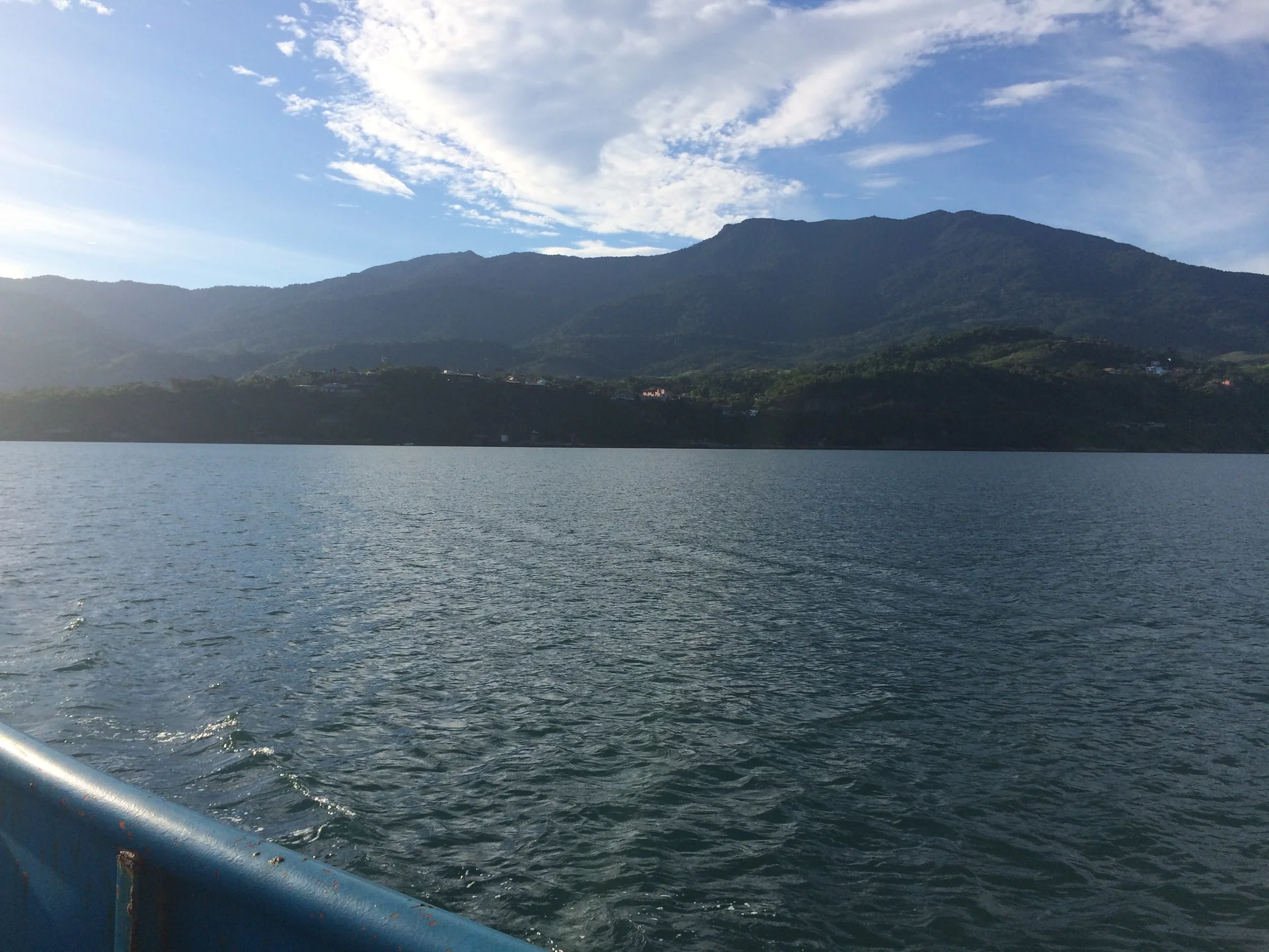 Vista do canal e do relevo verde de Ilhabela a partir da travessia de balsa em dia claro.