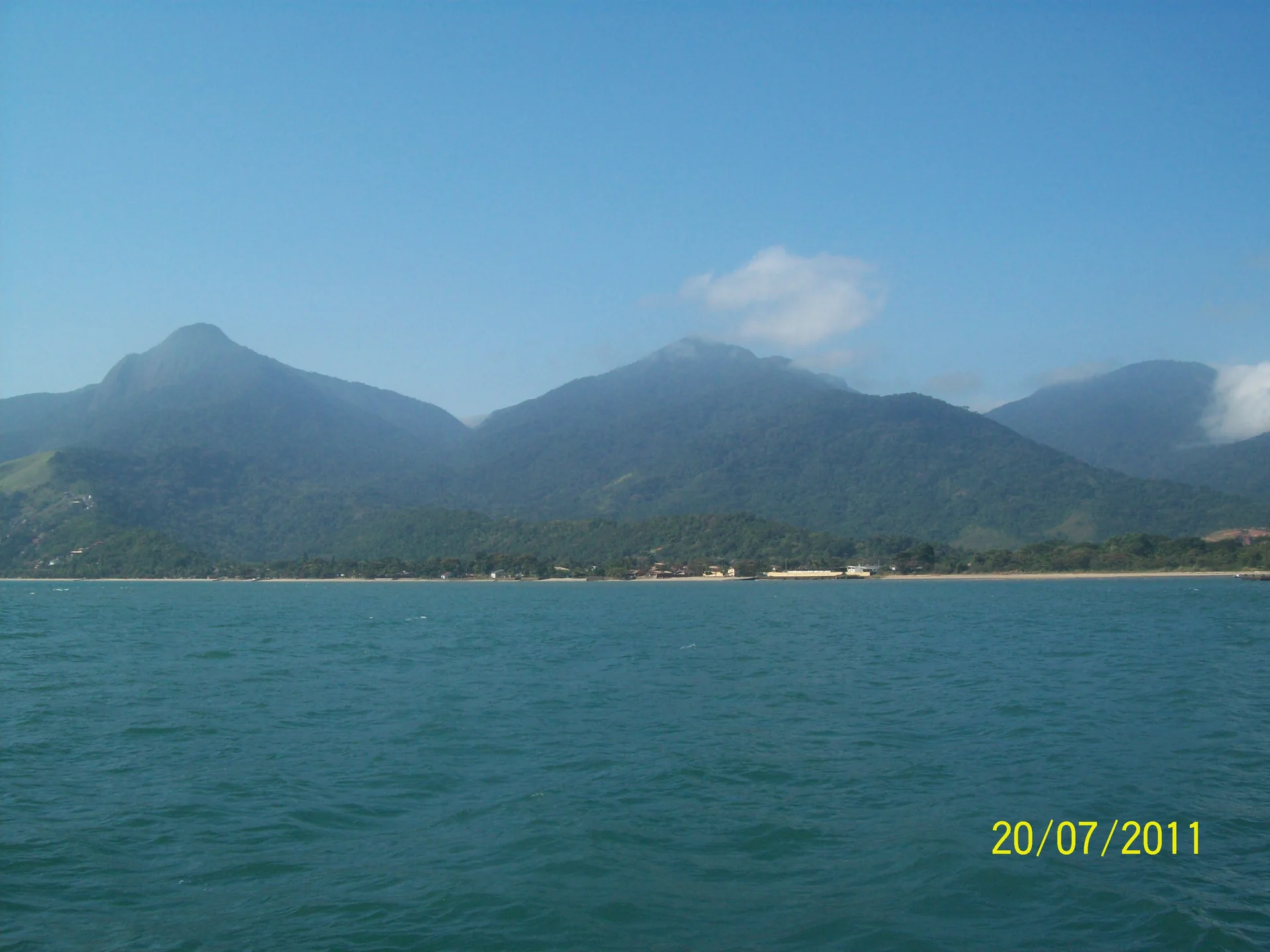 Ilhabela vista da balsa durante a aproximação da ilha, com mar azul e montanhas verdes ao fundo.