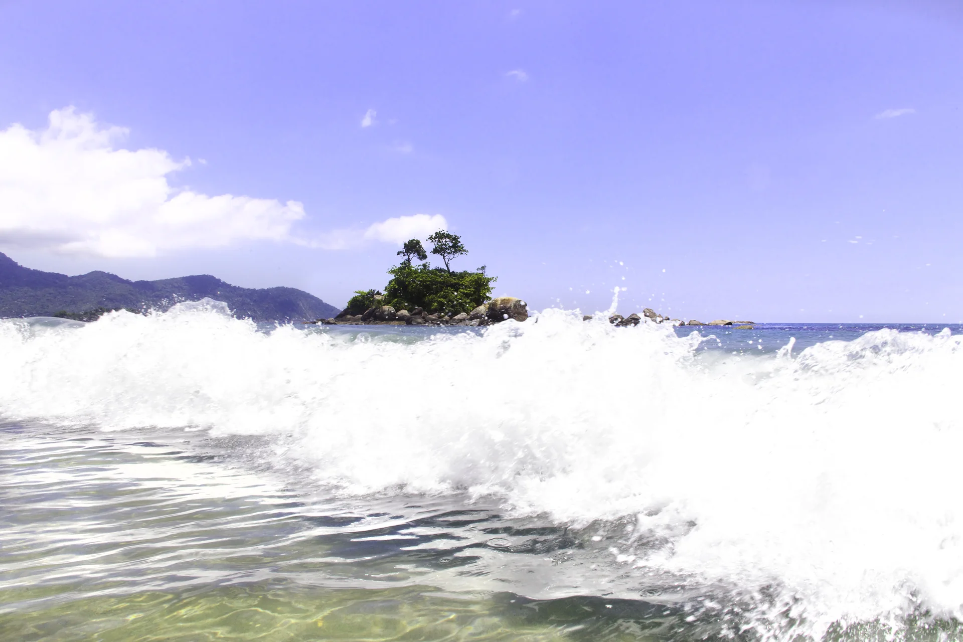 Praia de Castelhanos em Ilhabela, com faixa de areia, mar e encostas cobertas de Mata Atlântica sob luz do dia.