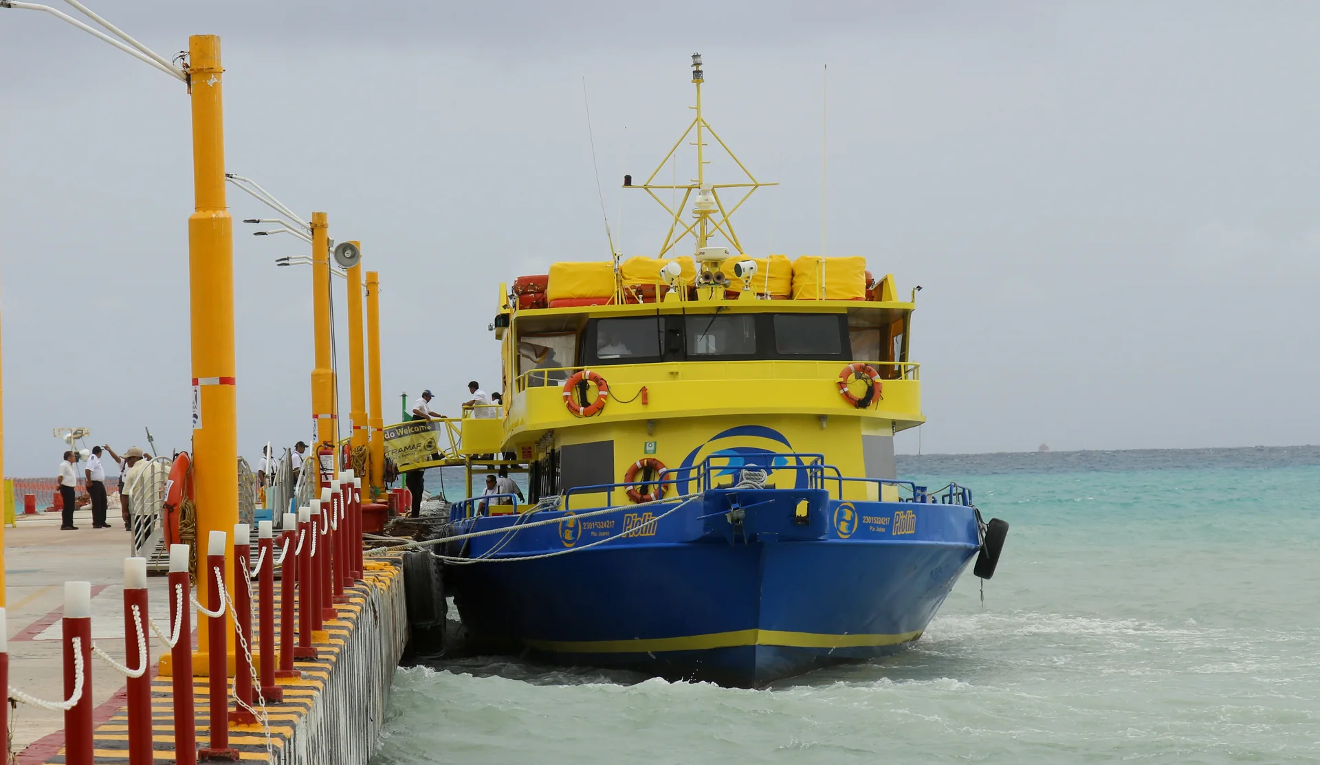 Ferry amarelo atracado em Playa del Carmen, com mar do Caribe ao lado do cais.