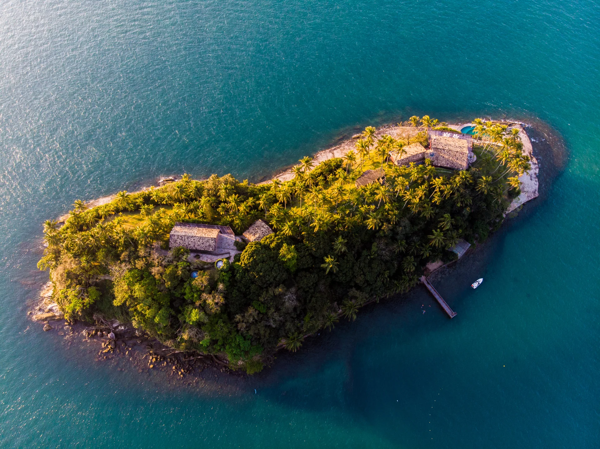 Vista aérea da Ilha das Cabras, cercada por água azul e vegetação, em Ilhabela.