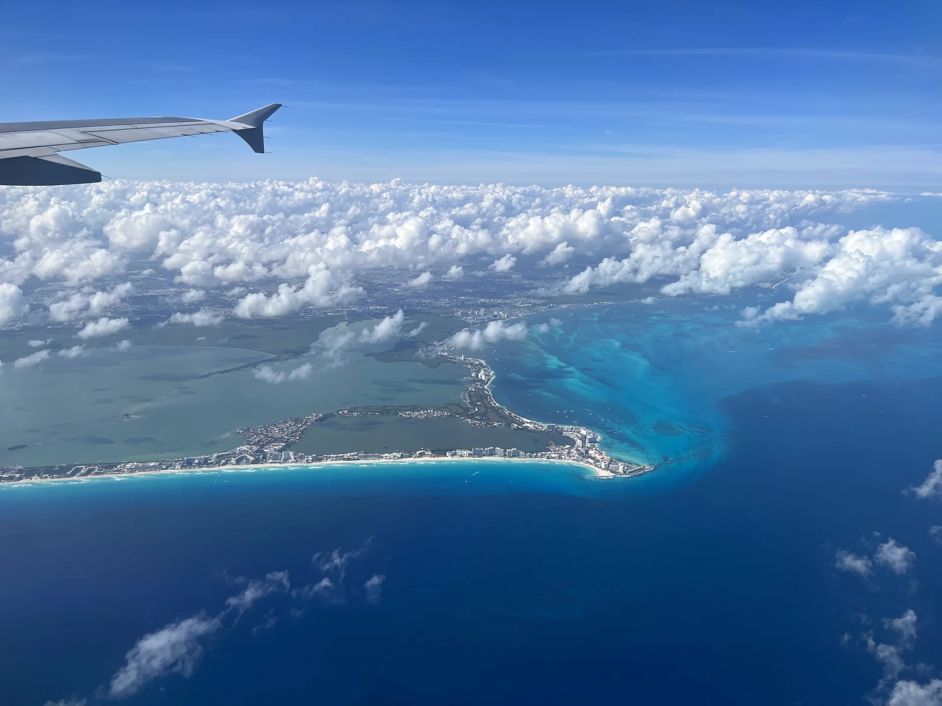 Vista aérea de Cancún a partir de avião, mostrando a faixa costeira, a lagoa e o Caribe em diferentes tons de azul.