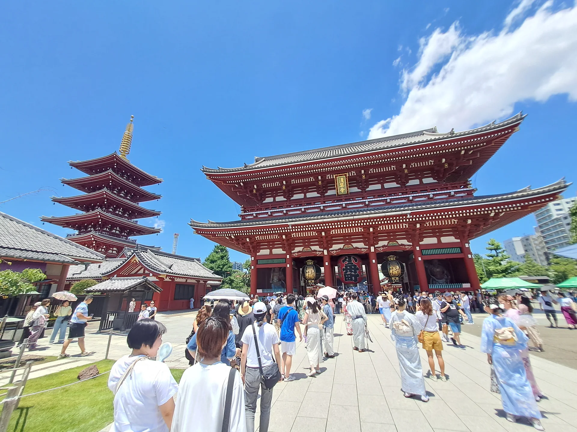 Portão Hōzōmon e pagode do templo Sensō-ji, em Asakusa, sob céu azul e com visitantes ao longe.