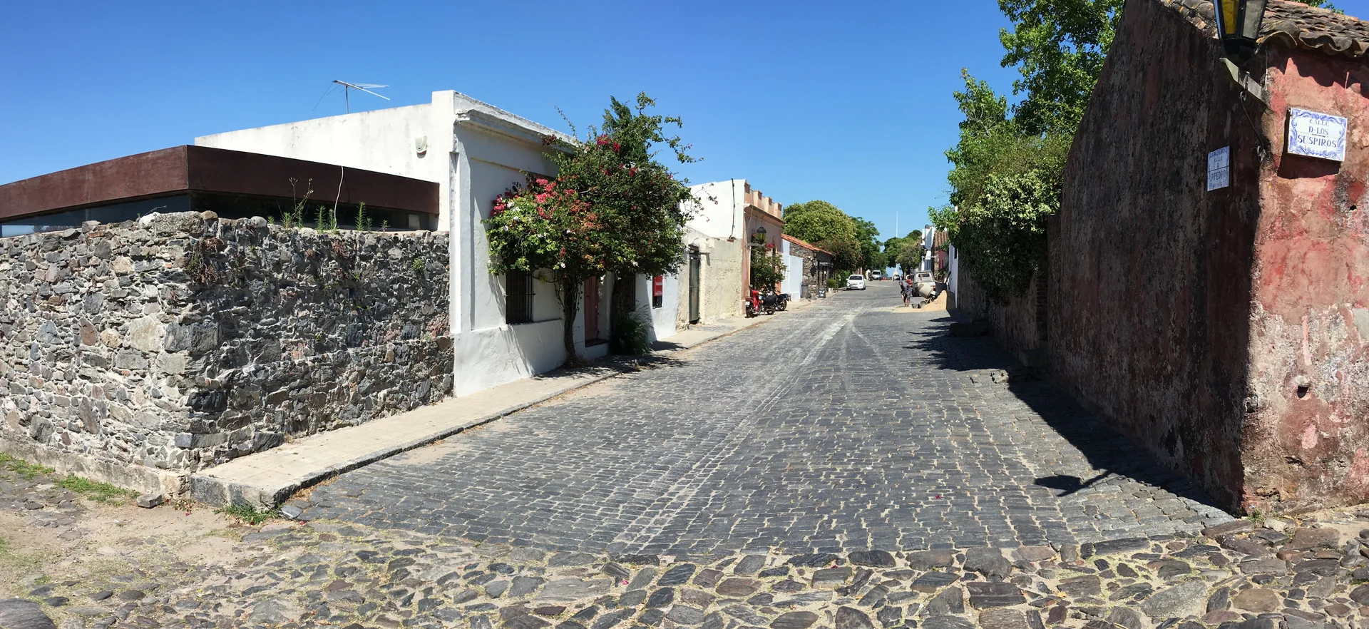 Rua de pedra do Bairro Histórico de Colônia do Sacramento, ladeada por casario baixo e árvores.