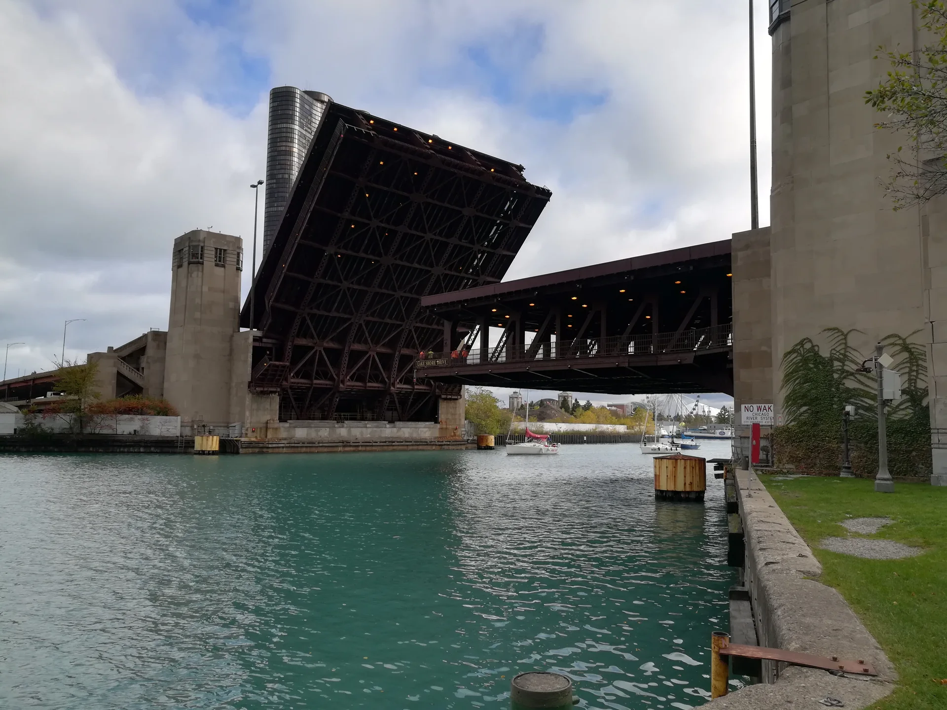 Ponte móvel elevada sobre o Chicago River, com estrutura de aço aparente, embarcações e edifícios sob luz diurna.