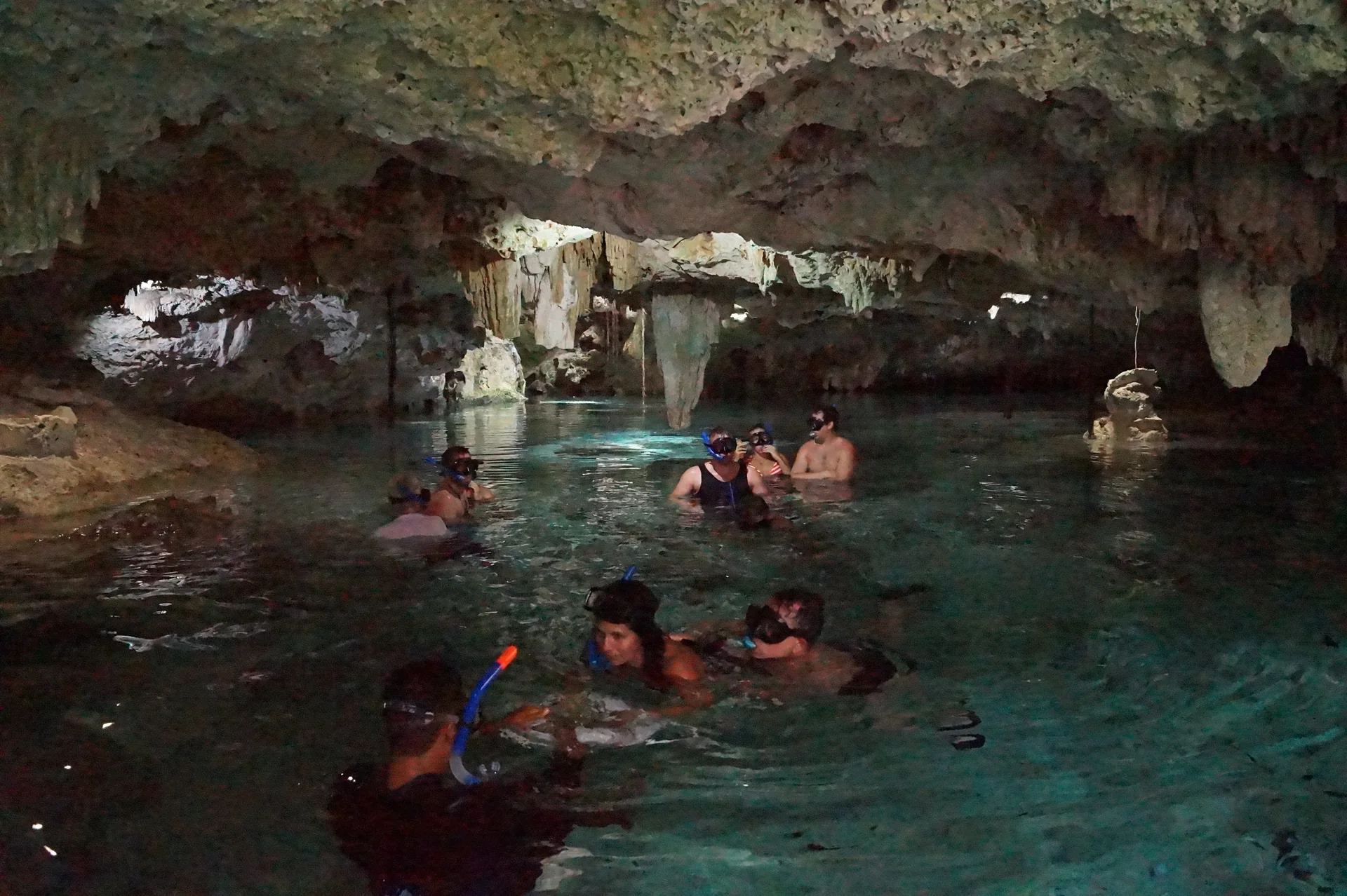 Visitantes usam máscaras de snorkel na área de água de um cenote em Aktun Chen, cercada por rocha calcária.