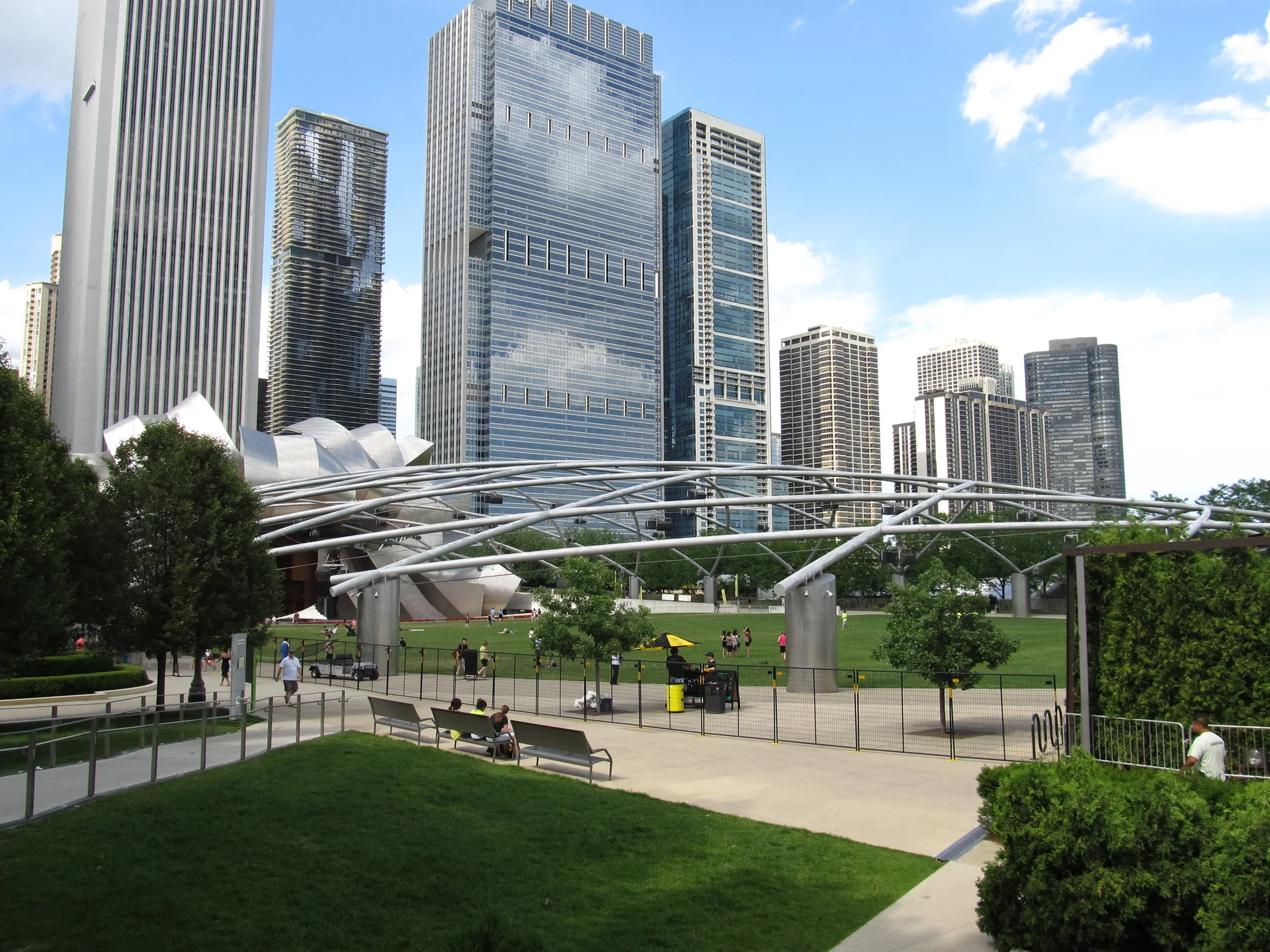 Jardim gramado e estrutura metálica do Jay Pritzker Pavilion em Millennium Park, diante de edifícios do Loop sob céu claro.