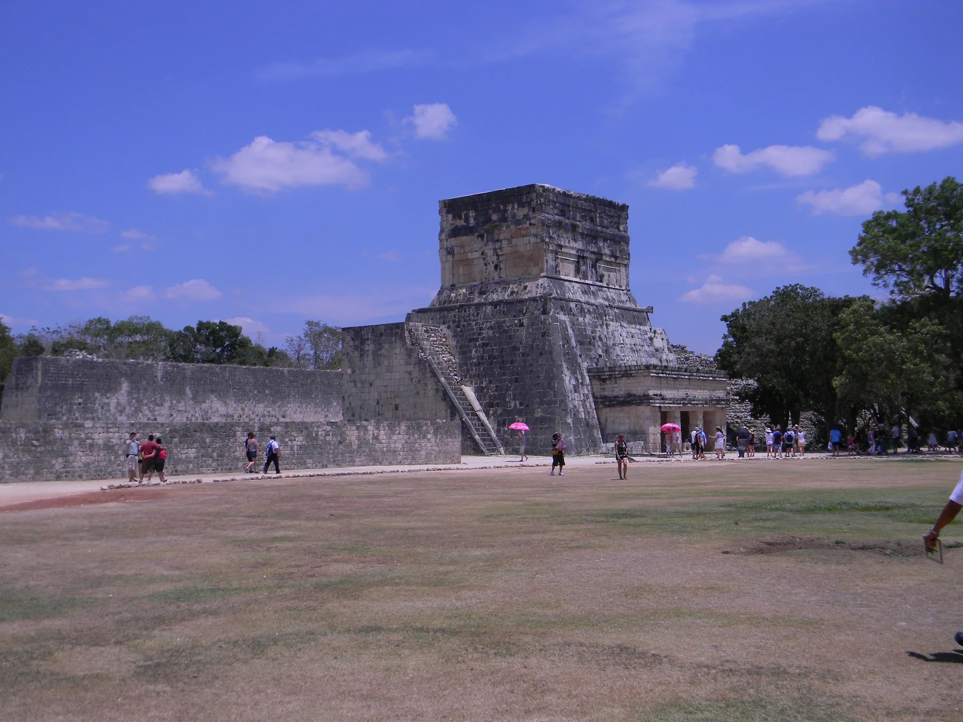 Entrada do Grande Jogo de Bola de Chichén Itzá, com paredes de pedra, visitantes distantes e céu azul em dia claro.