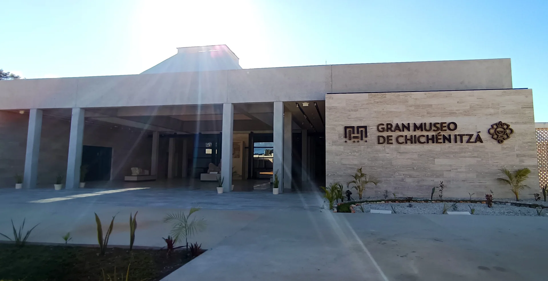 Entrada do Gran Museo de Chichén Itzá em edifício contemporâneo, com letreiro no muro de pedra e luz do sol.