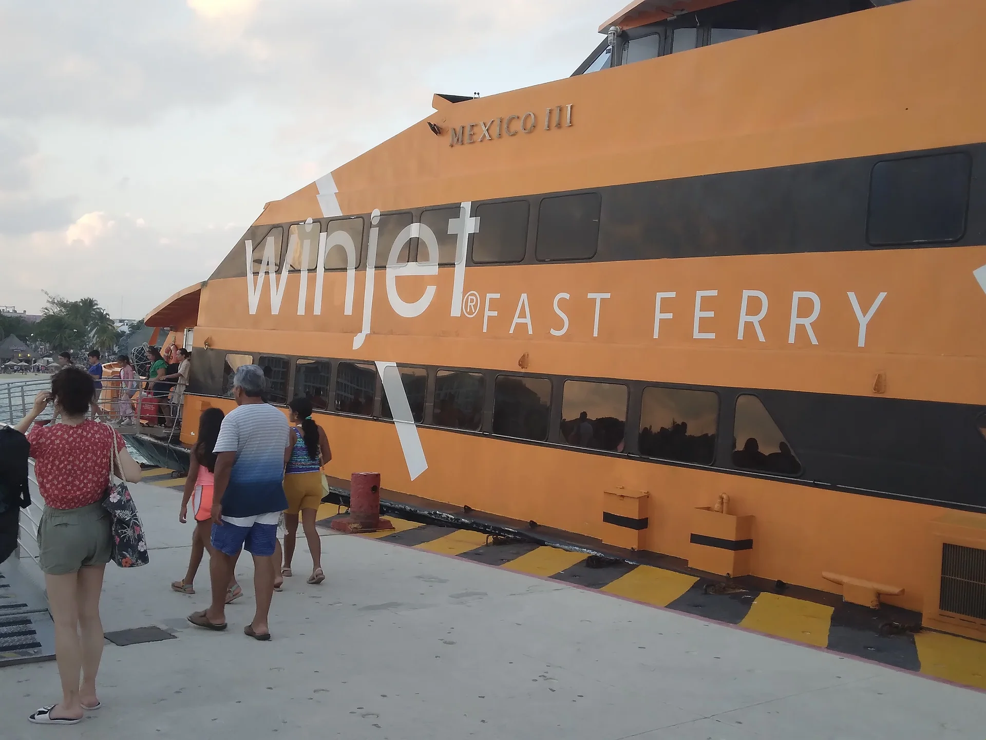Passageiros caminham pelo píer para embarcar no ferry Winjet em Playa del Carmen, durante o dia.