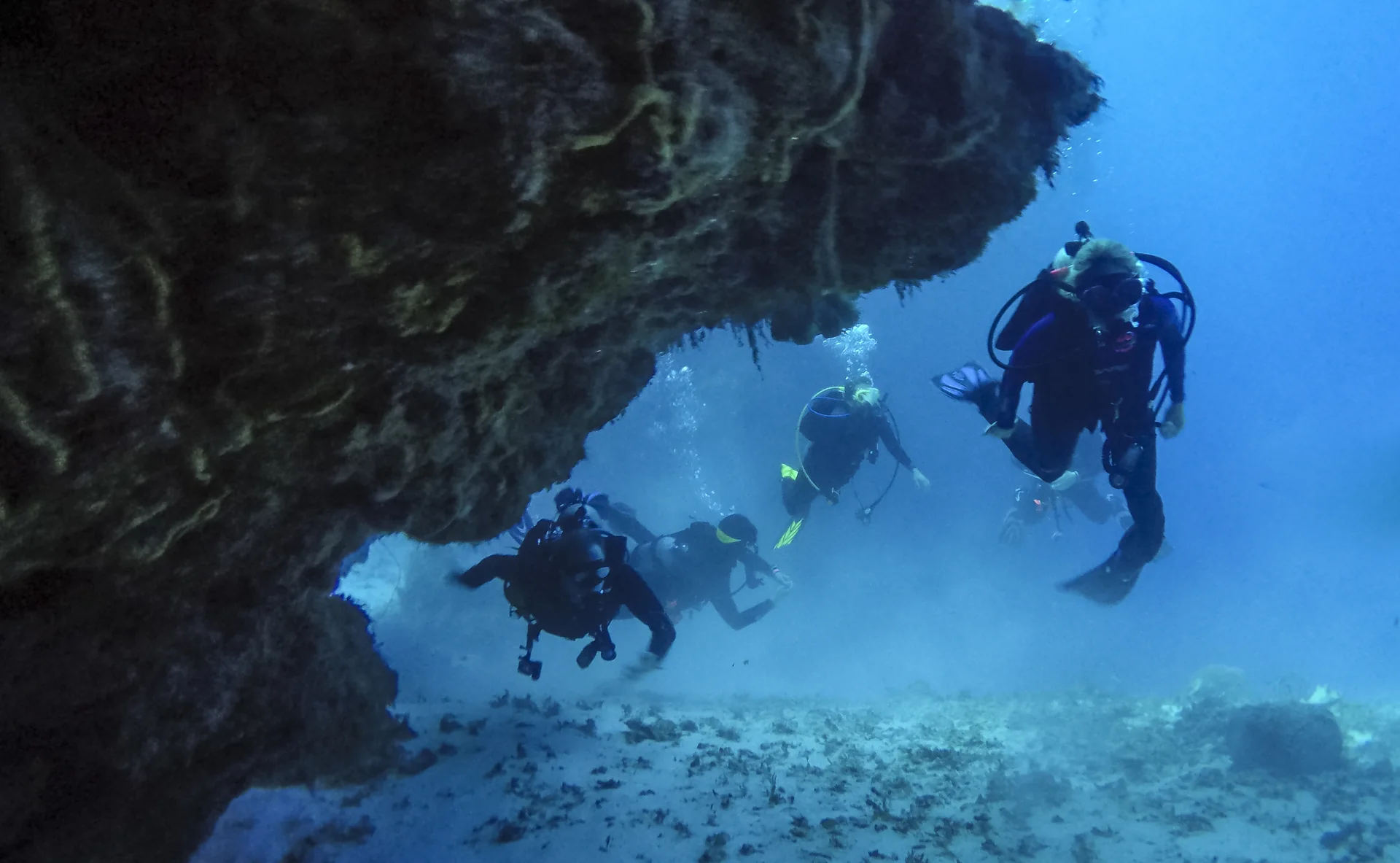 Grupo de mergulhadores com cilindro atravessa uma formação de coral em Cozumel, mantendo-se suspenso acima do fundo.