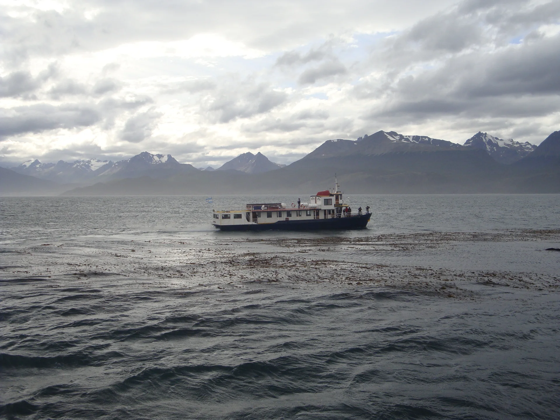 Embarcação atravessando o Canal de Beagle, com água azul e montanhas da Terra do Fogo no horizonte.