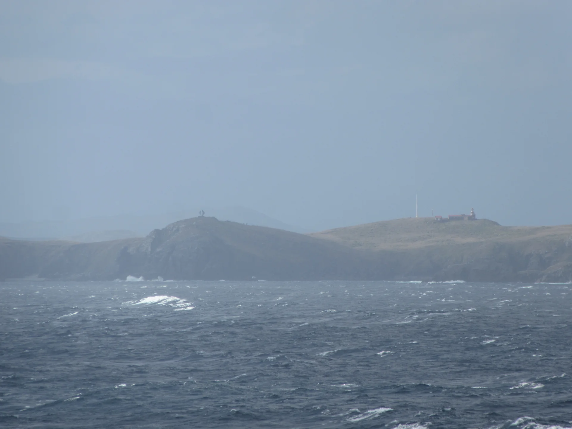 Monumento do Albatroz e farol no Cabo de Hornos vistos sob luz natural em paisagem marítima remota.