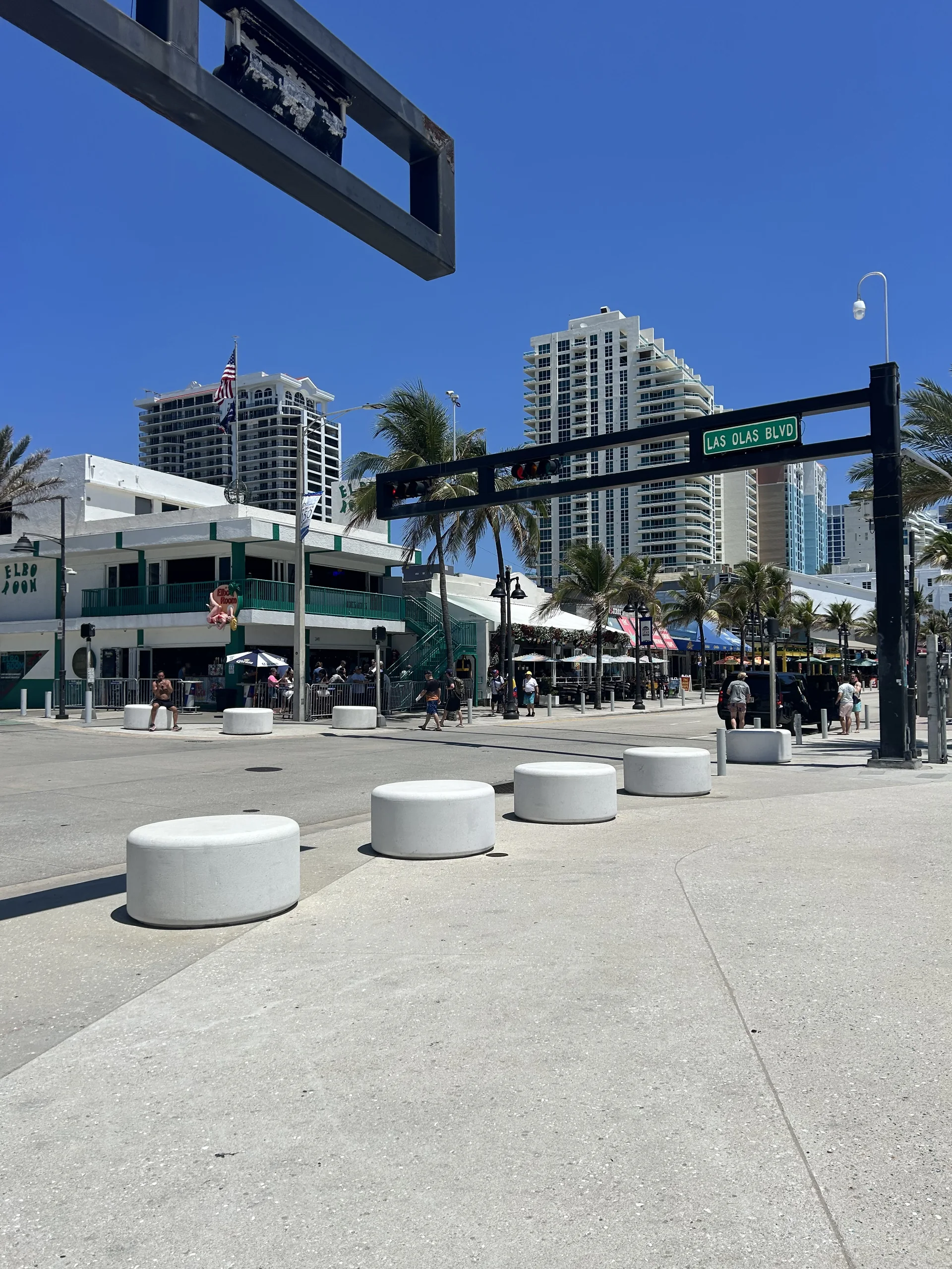 Cruzamento da Las Olas Boulevard em Fort Lauderdale com placa da avenida, palmeiras, calçadas e edifícios sob sol intenso.
