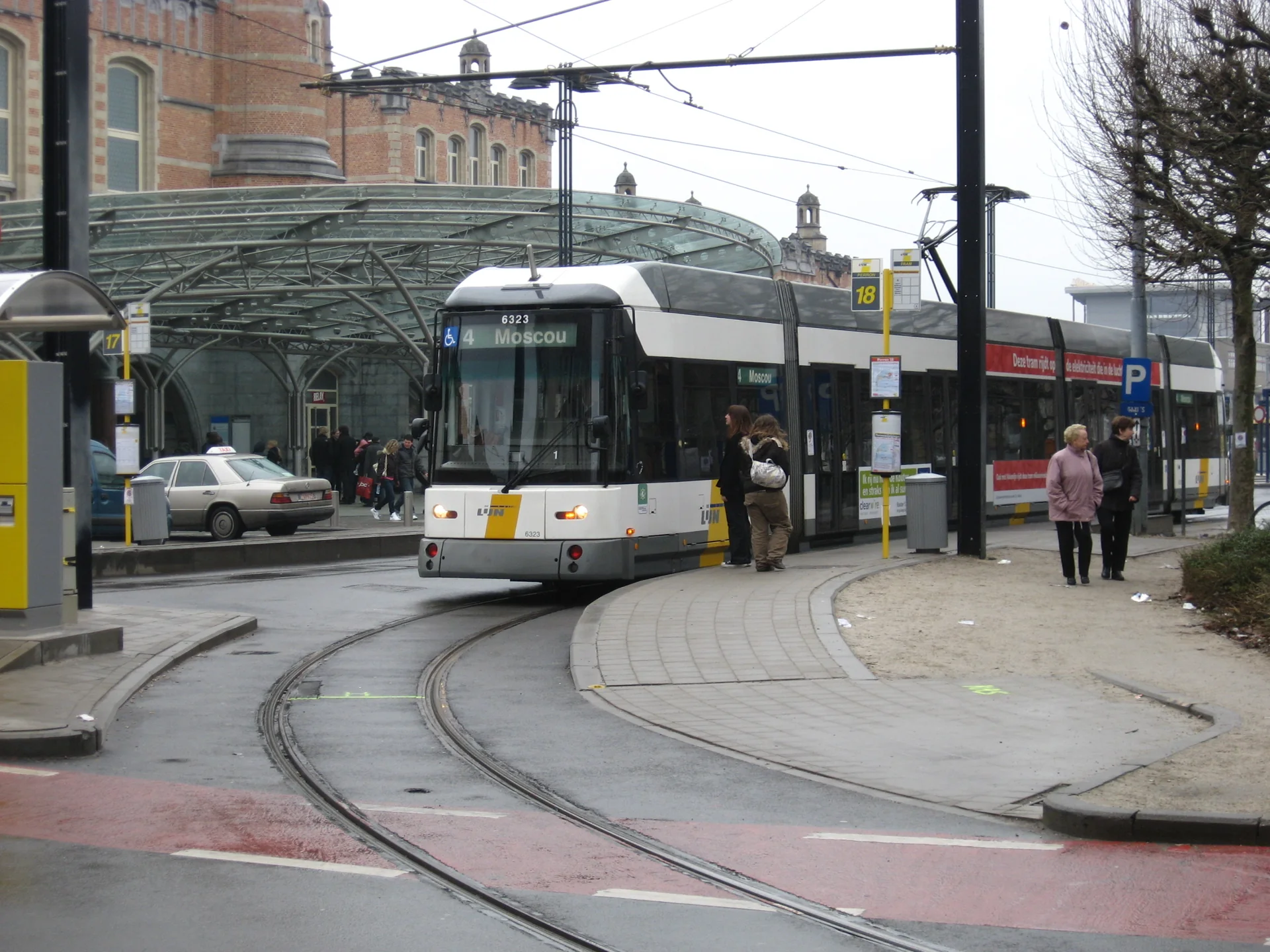 Bonde da De Lijn junto à estação Gent-Sint-Pieters, com plataforma e passageiros em contexto urbano.