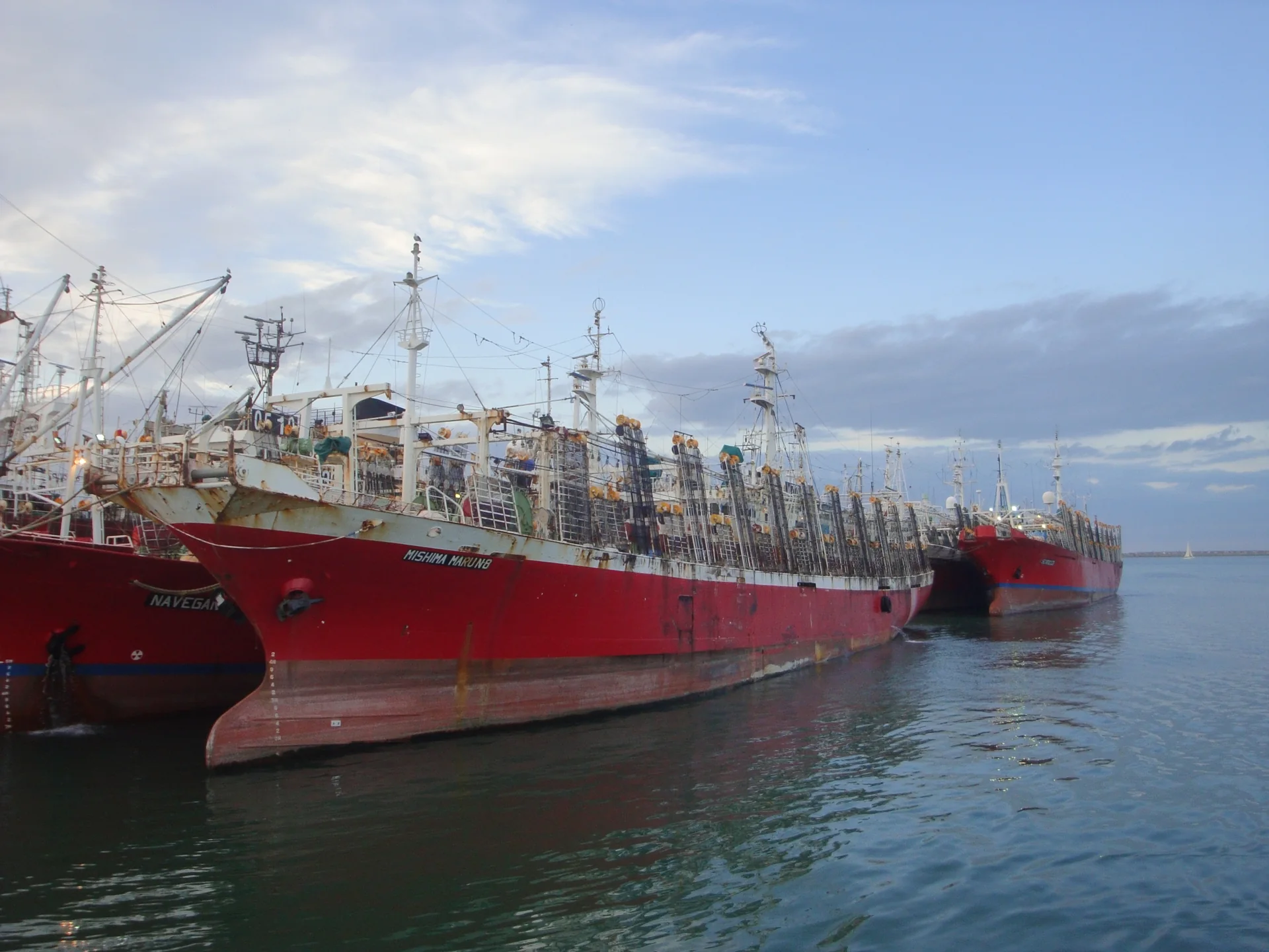 Barcos de pesca vermelhos atracados no porto de Mar del Plata, com mastros, redes e céu claro sobre a água.