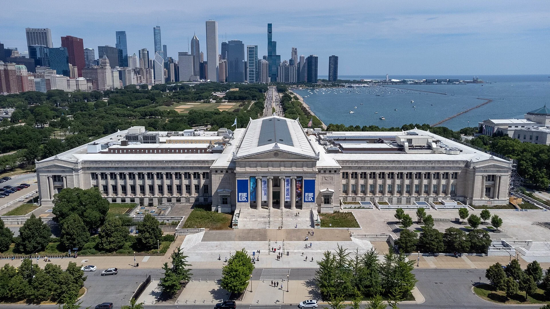 Vista aérea do Field Museum em dia claro, com o skyline de Chicago, áreas verdes e o Lake Michigan ao fundo.