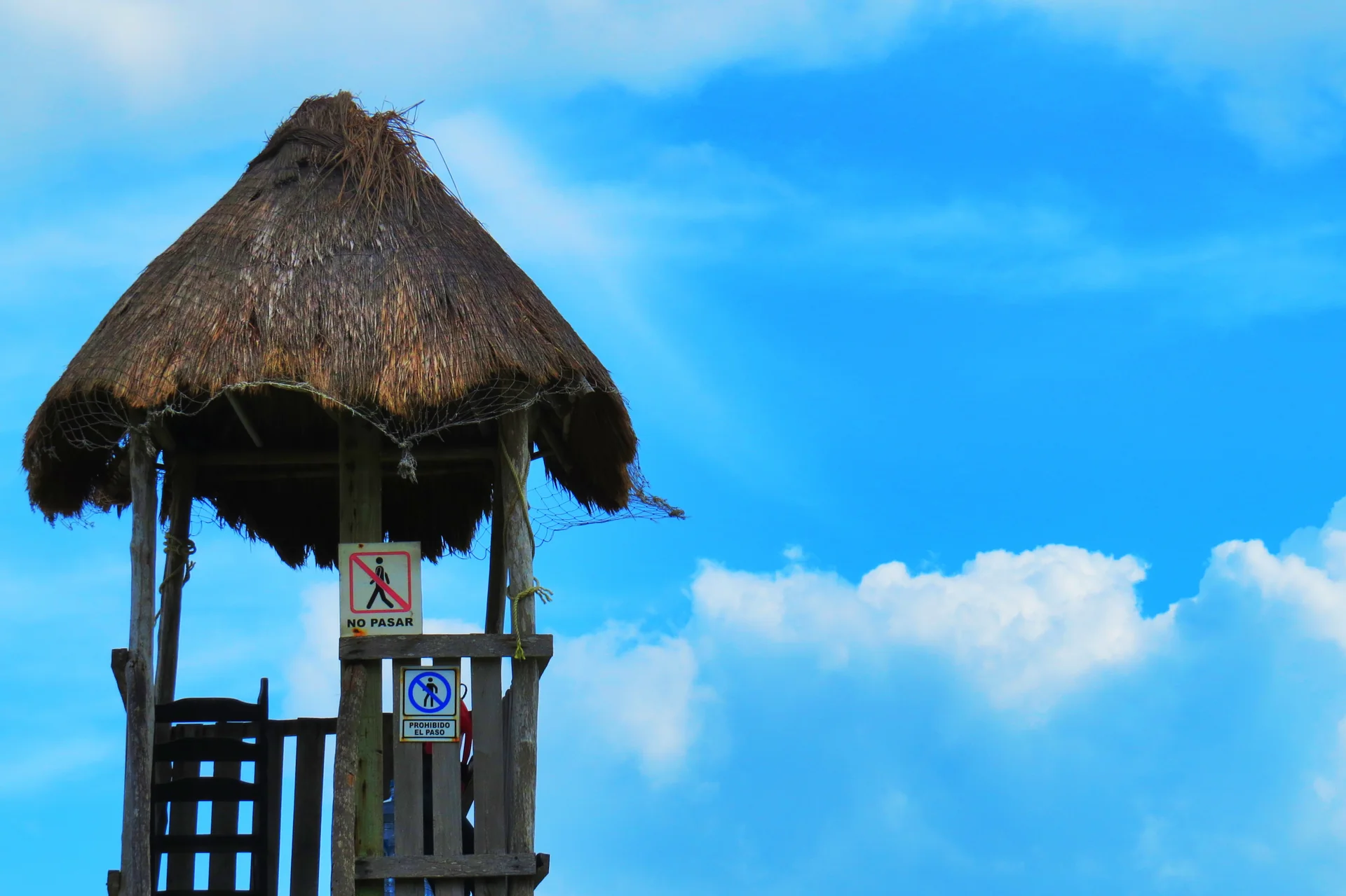 Torre de salva-vidas com placas de acesso em Playa Coral, Cancún, diante de céu azul com nuvens.
