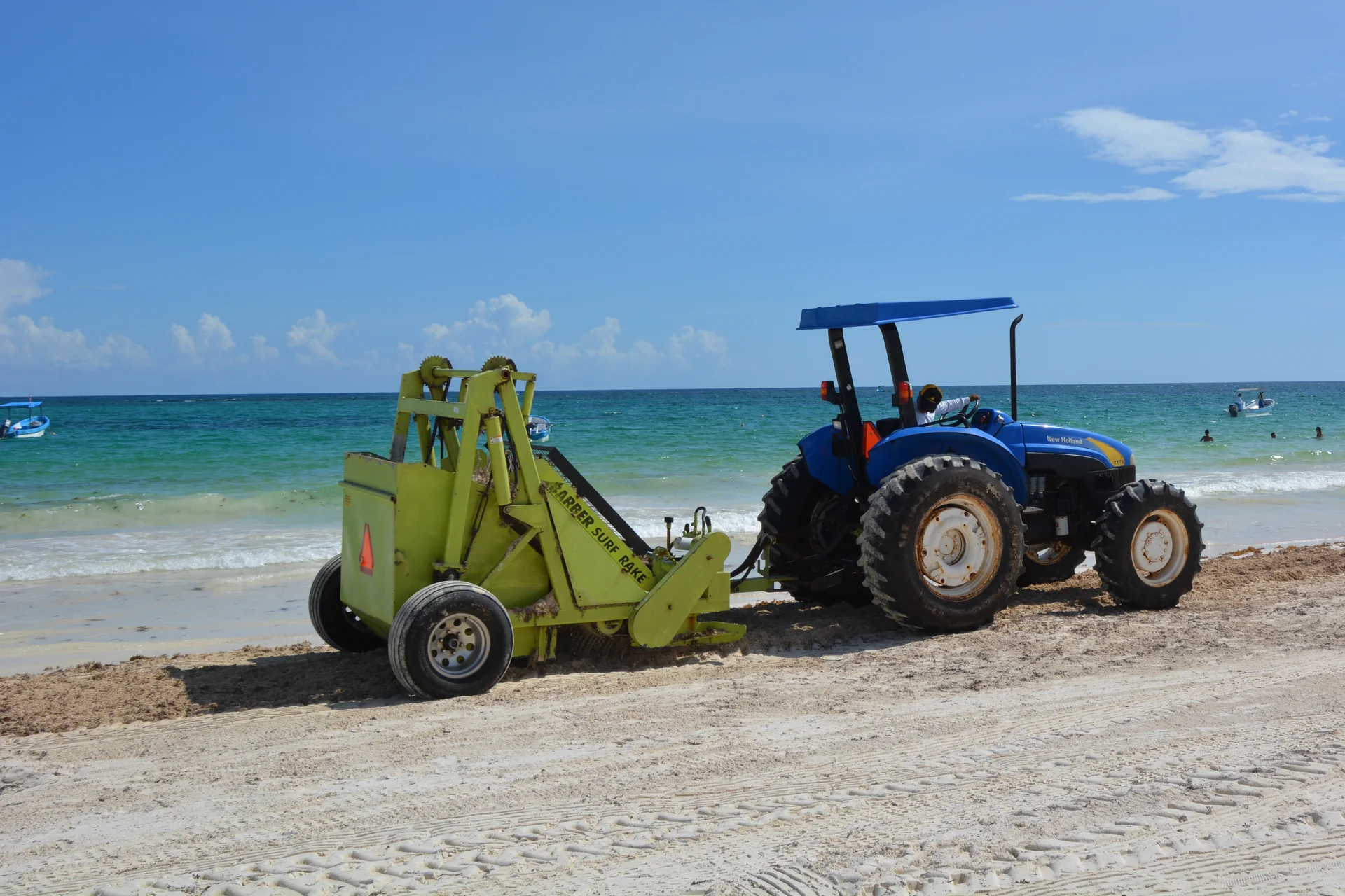 Trator com equipamento de limpeza na praia de Tulum, com mar do Caribe ao fundo, em operação de remoção de sargaço.