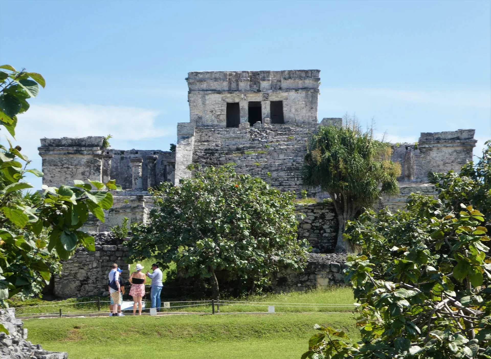 El Castillo de Tulum visto de área de visitação, com escadaria de pedra e vegetação sob luz do dia.