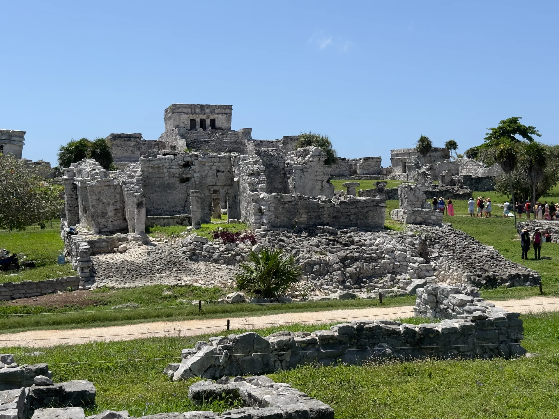 Estruturas de pedra da Zona Arqueológica de Tulum vistas em um dia claro a partir do percurso de visitação.
