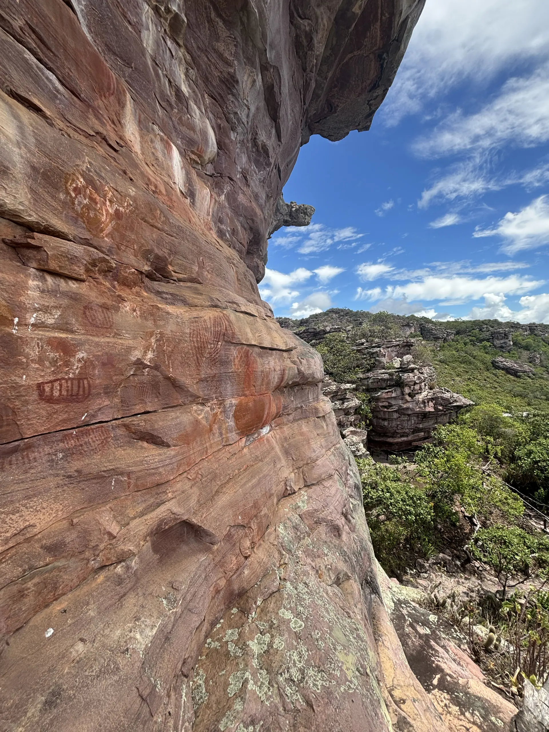 Pinturas rupestres na Serra das Paridas, na Chapada Diamantina, em parede de arenito ao lado de afloramentos e vegetação sob céu claro.