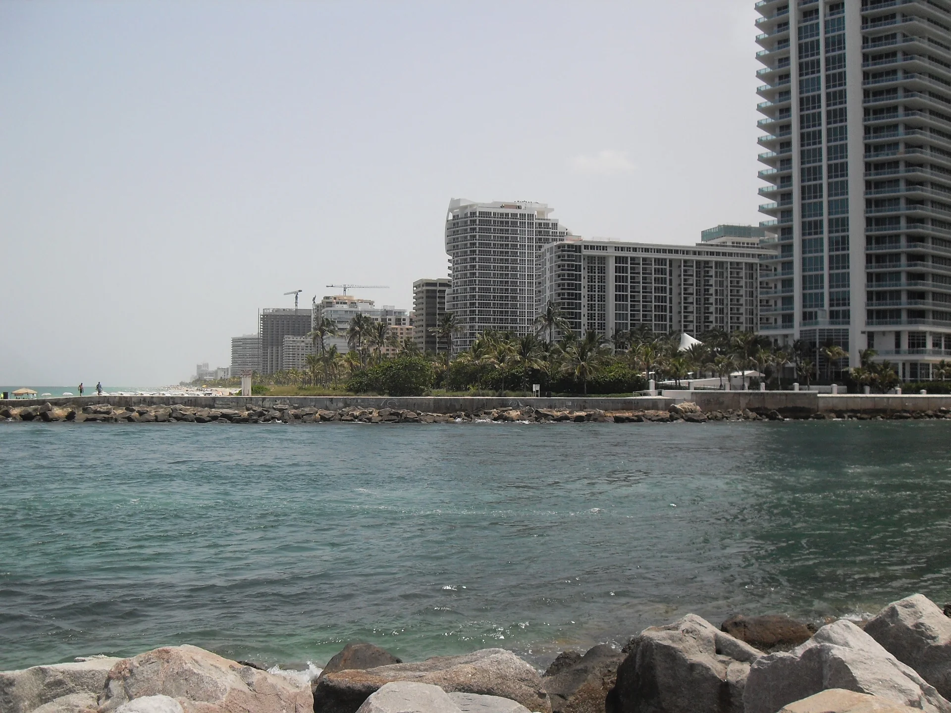 Baker’s Haulover Inlet visto do Haulover Park, com rochas em primeiro plano e edifícios da faixa costeira de Bal Harbour ao fundo.