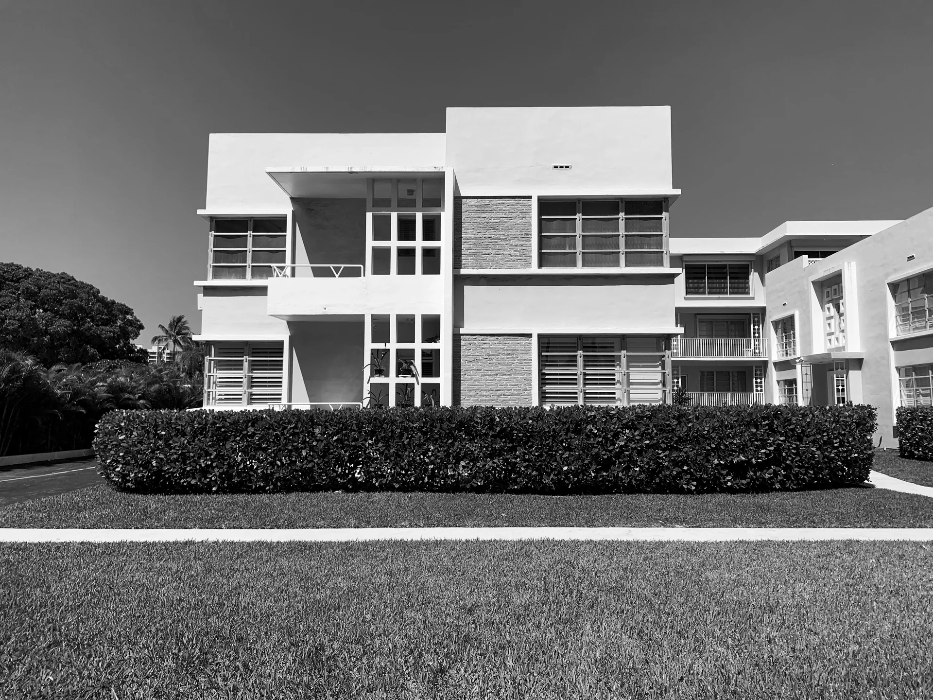 Edifício residencial modernista de 1950 em Bal Harbour, com volumes brancos, janelas horizontais e paisagismo frontal, em fotografia em preto e branco.