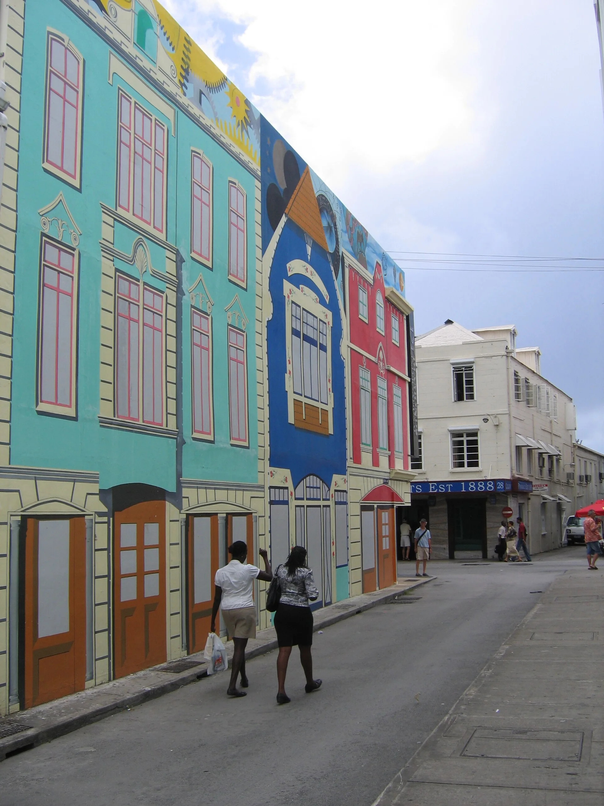 Fachadas coloridas e pintura mural em Bolton Lane, no centro de Bridgetown, com pedestres ao fundo sob luz do dia.