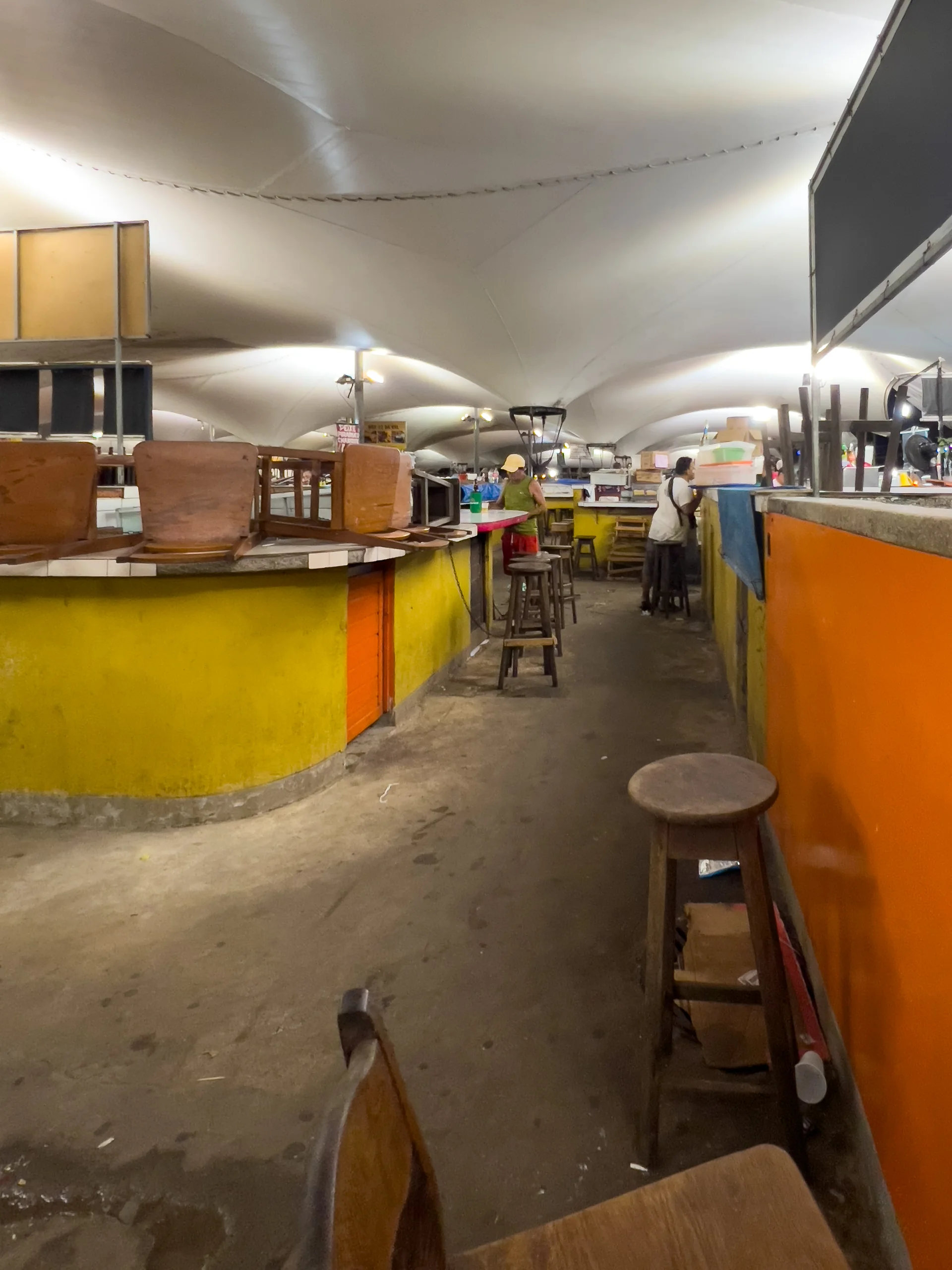 Corredor interno do Mercado Ver-o-Peso em Belém, com balcões coloridos, bancos e circulação de pessoas ao fundo.
