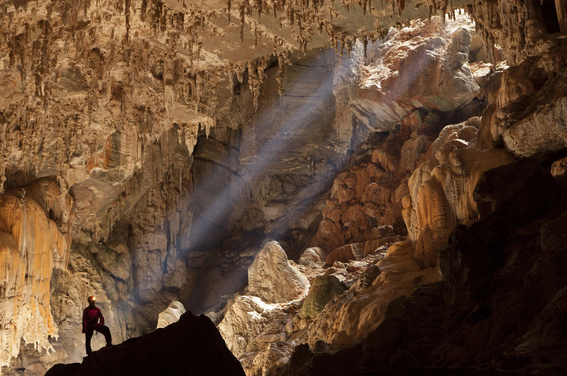 Espeleólogo de capacete observa raios de sol sob uma claraboia no interior da Caverna Terra Ronca, entre espeleotemas.