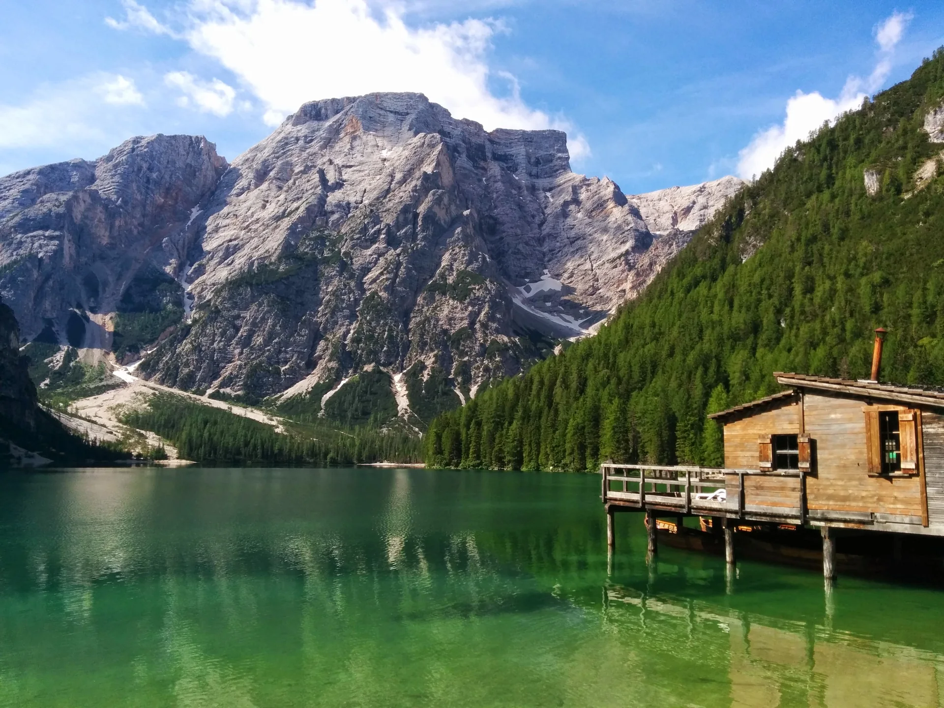 Lago alpino nas Dolomitas visto de margem autorizada, com água azul-esverdeada, montanhas rochosas e luz natural clara.