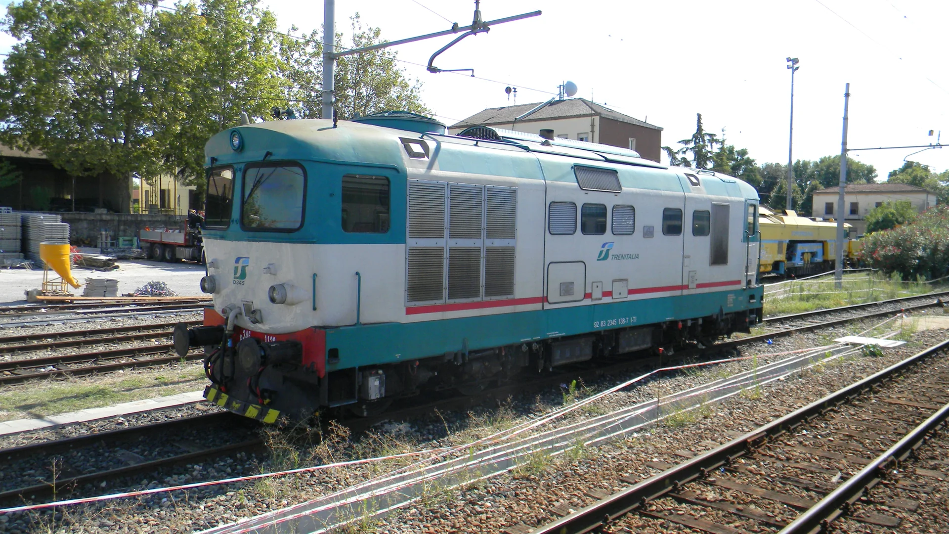 Locomotiva da Trenitalia parada na estação de Peschiera del Garda, com trilhos e rede aérea sob luz diurna.