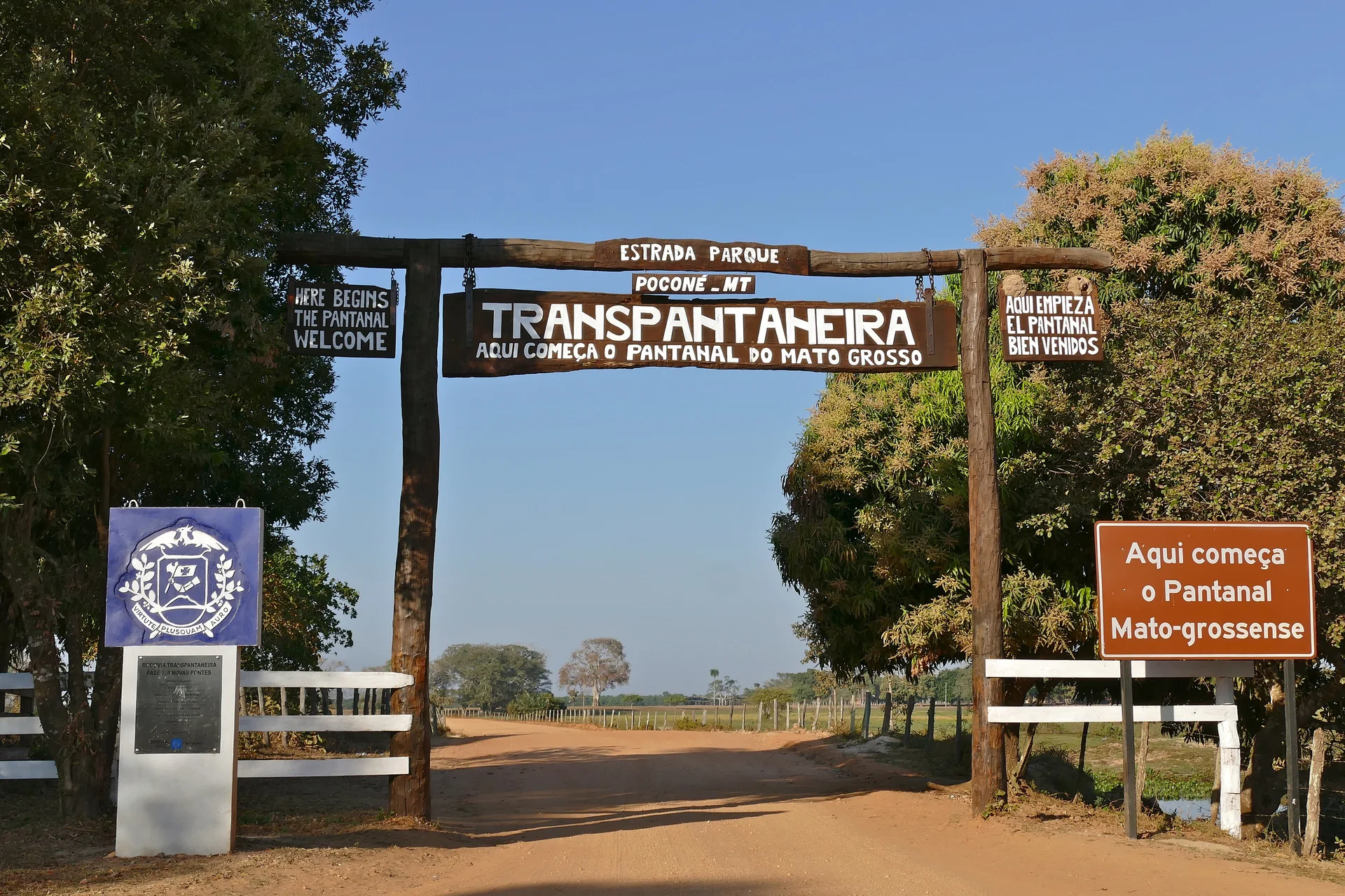 Pórtico de madeira da Estrada Parque Transpantaneira, em Poconé, com placas que indicam o começo do Pantanal mato-grossense sob céu azul.
