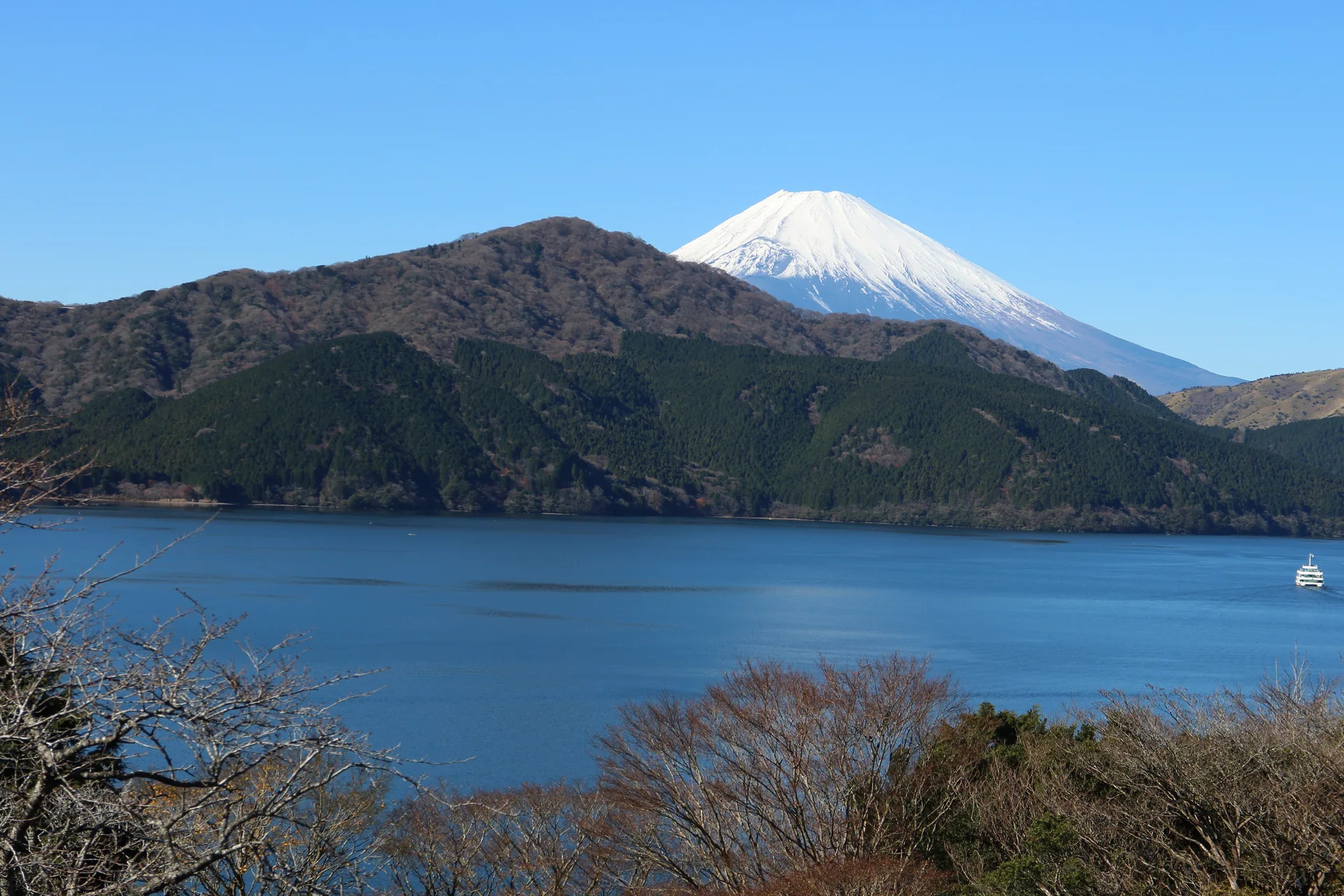 Lago Ashi em Hakone com encostas arborizadas, um barco ao longe e o Monte Fuji ao fundo sob céu claro.