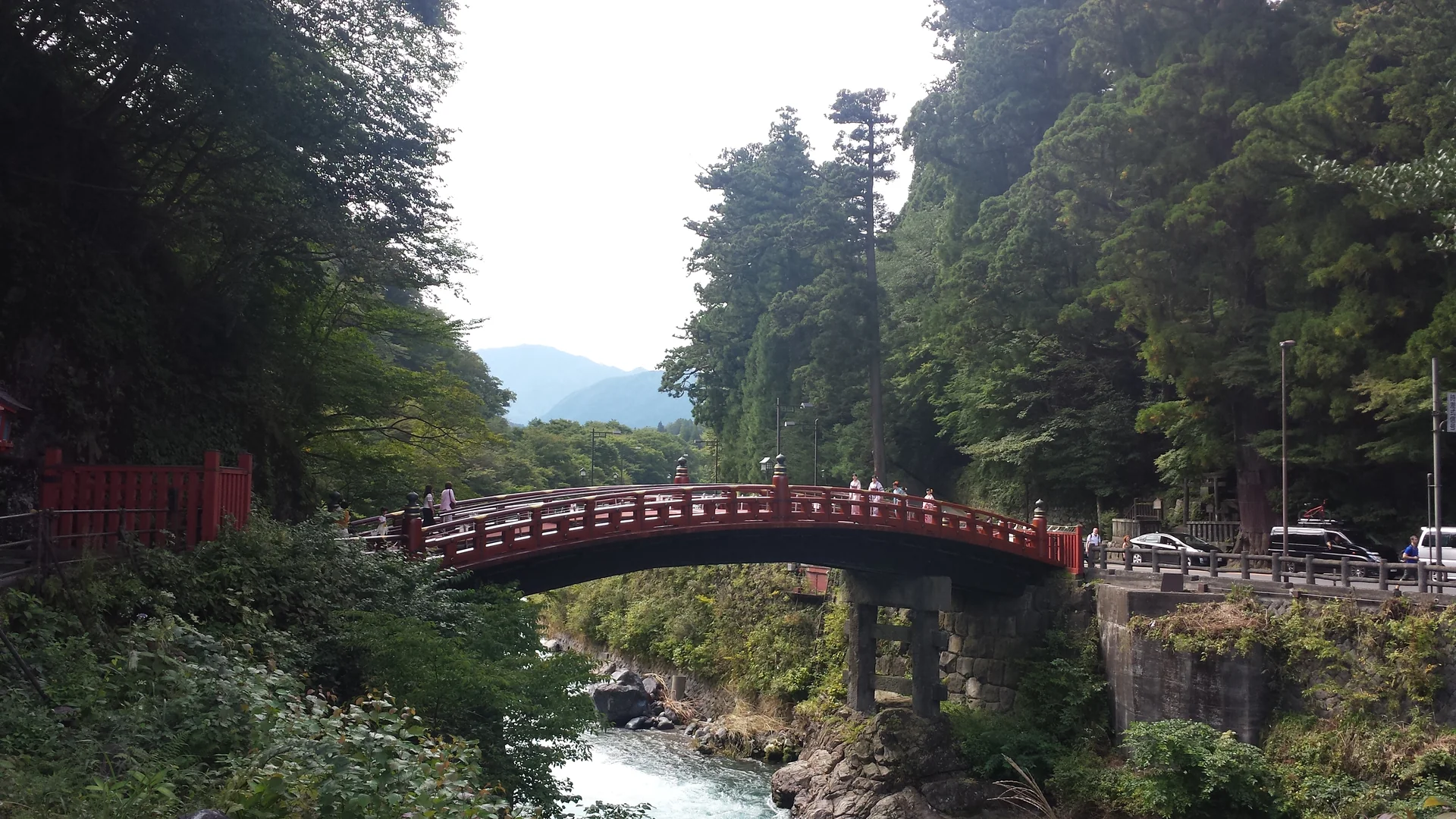 Ponte Shinkyo de madeira vermelha sobre o rio, cercada pela floresta de Nikko em luz diurna.