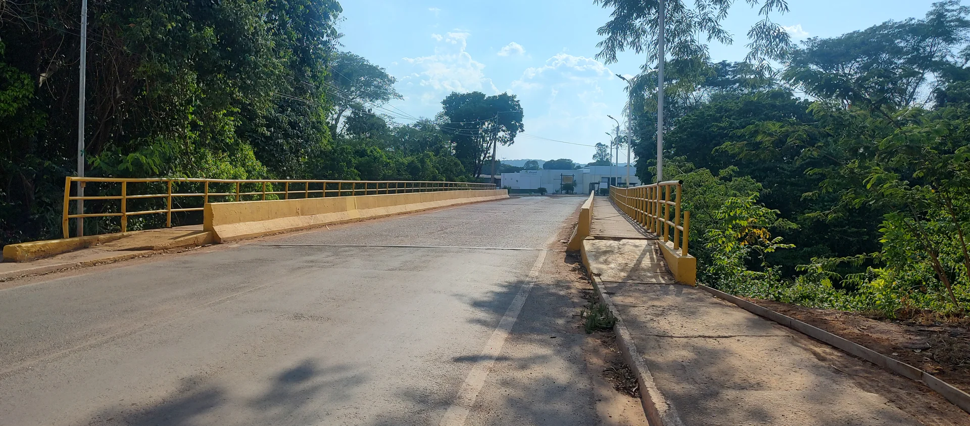 Ponte sobre o Rio Nobres no Jardim Petrópolis, com via asfaltada, guarda-corpo amarelo e vegetação nas margens.