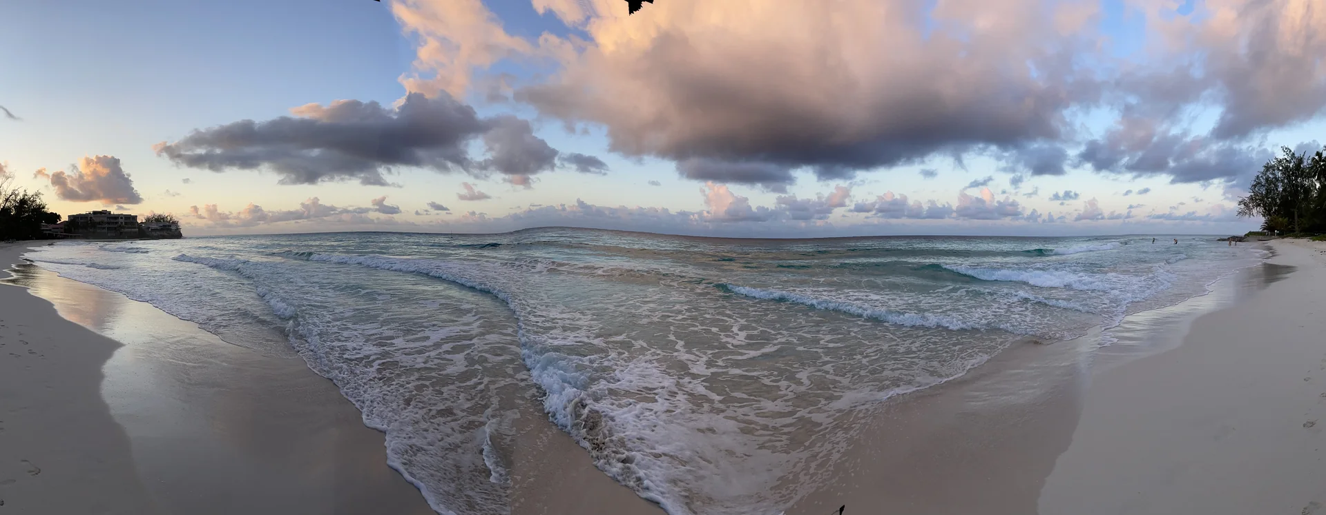 Vista panorâmica de Accra Beach, em Barbados, com ondas baixas quebrando sobre areia clara sob céu com nuvens.