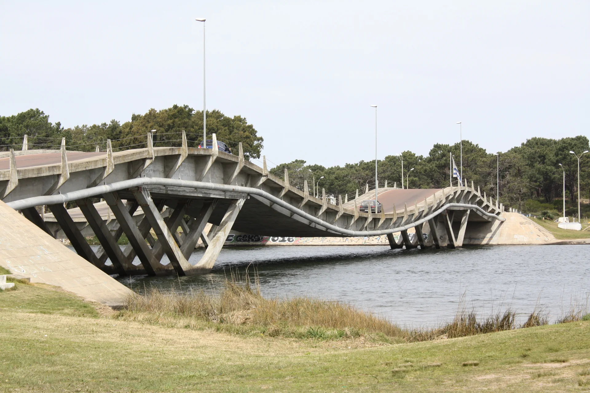 Ponte ondulante de La Barra sobre o Arroyo Maldonado, com vegetação nas margens e veículos atravessando em luz diurna.