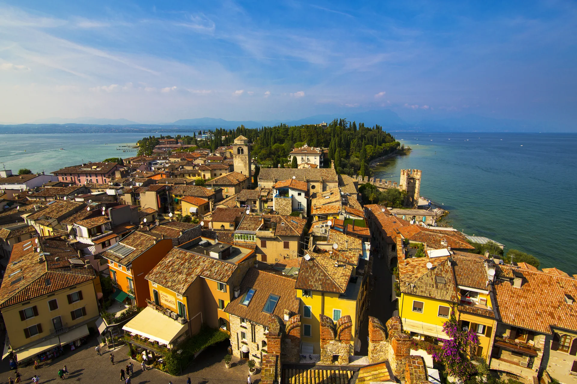 Península de Sirmione vista em dia claro, com telhados do centro histórico, vegetação e o Lago di Garda ao redor.