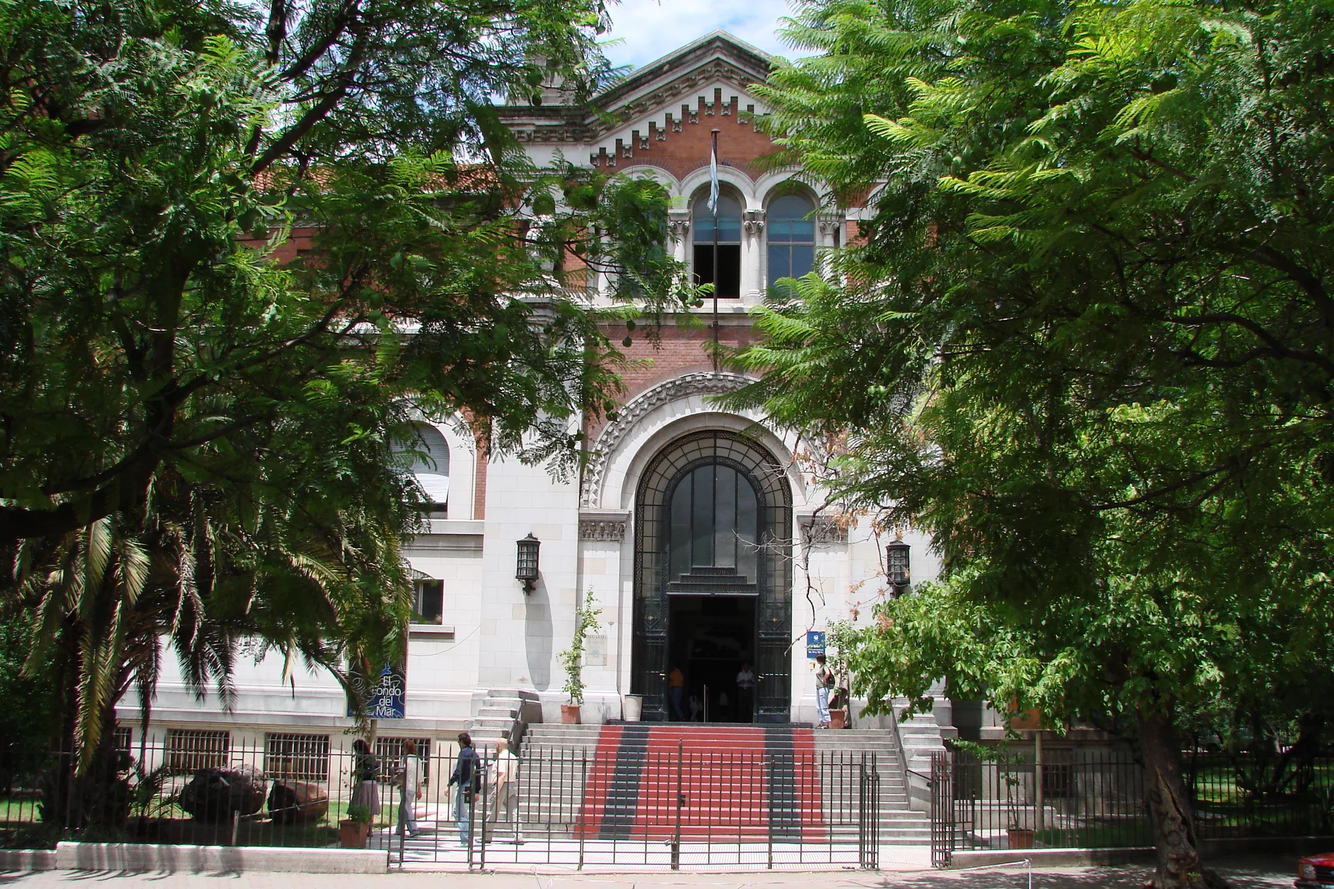 Fachada histórica do Museo Argentino de Ciencias Naturales Bernardino Rivadavia, enquadrada por árvores do Parque Centenario em dia claro.
