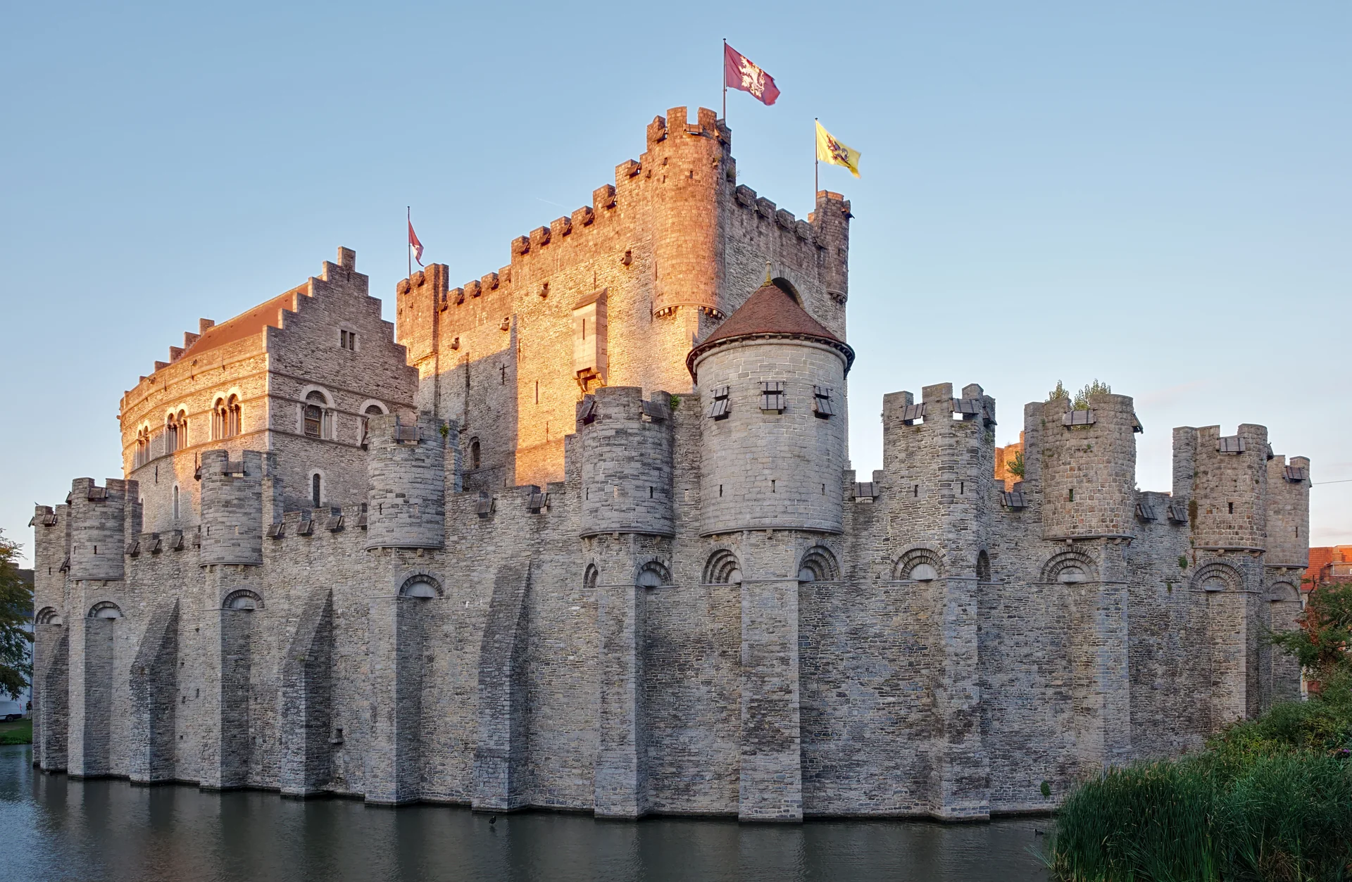 Fachada de pedra do Castelo Gravensteen, com fosso e muralhas, no centro histórico de Gante sob luz natural.