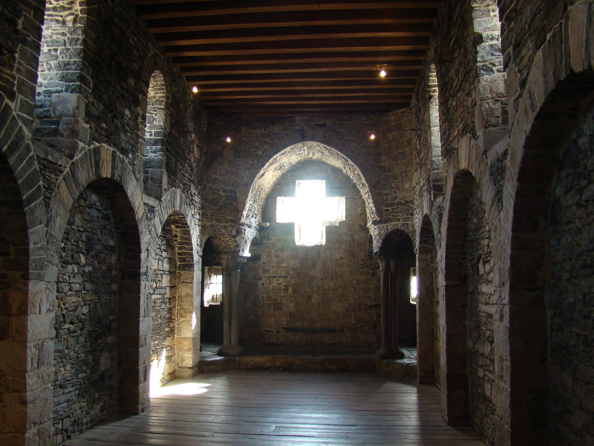 Interior de pedra do Castelo Gravensteen, com arcadas, teto de madeira e luz entrando pela janela.