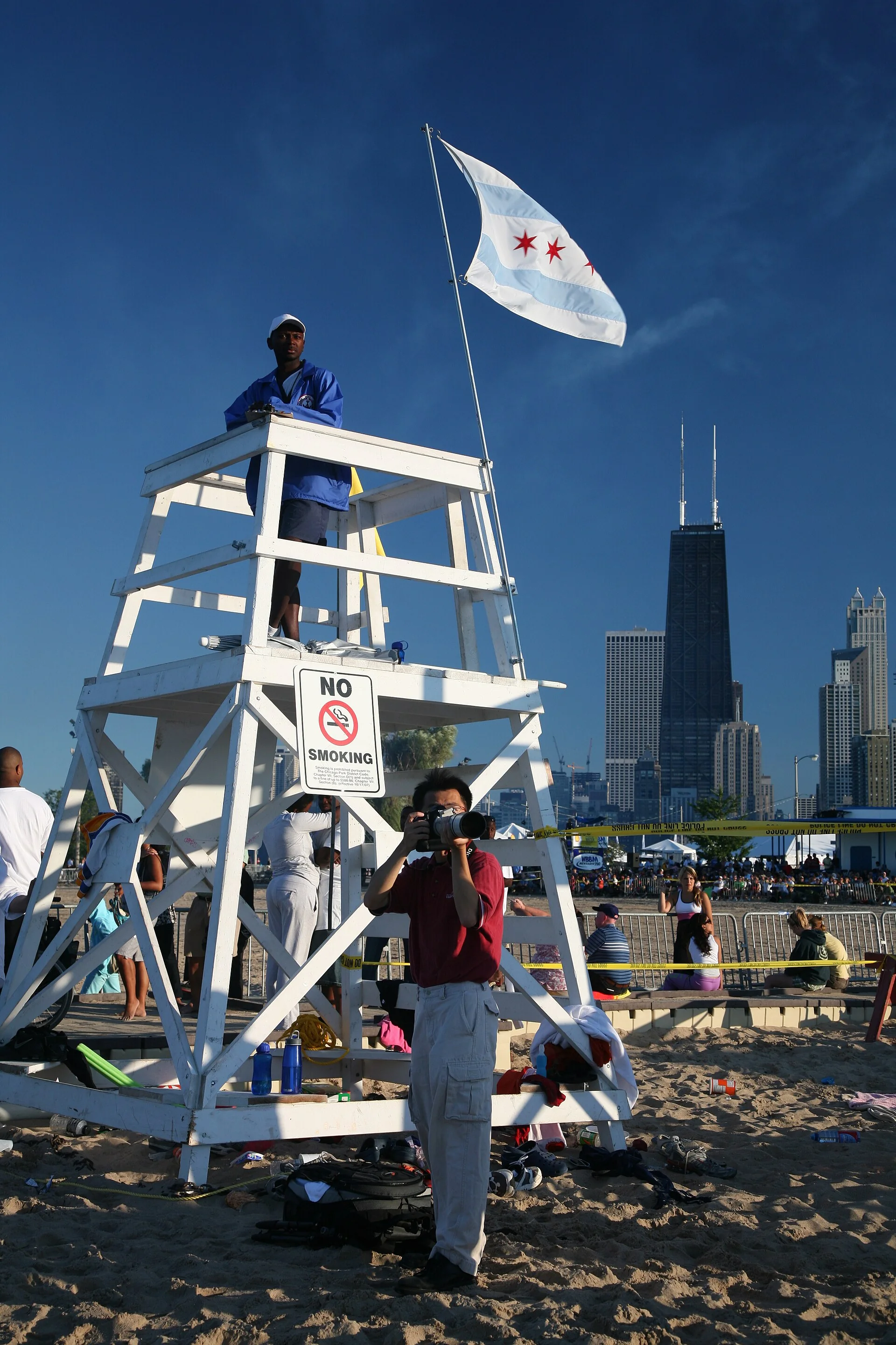 Salva-vidas em posto elevado de North Avenue Beach, com a bandeira de Chicago, areia e edifícios ao fundo.