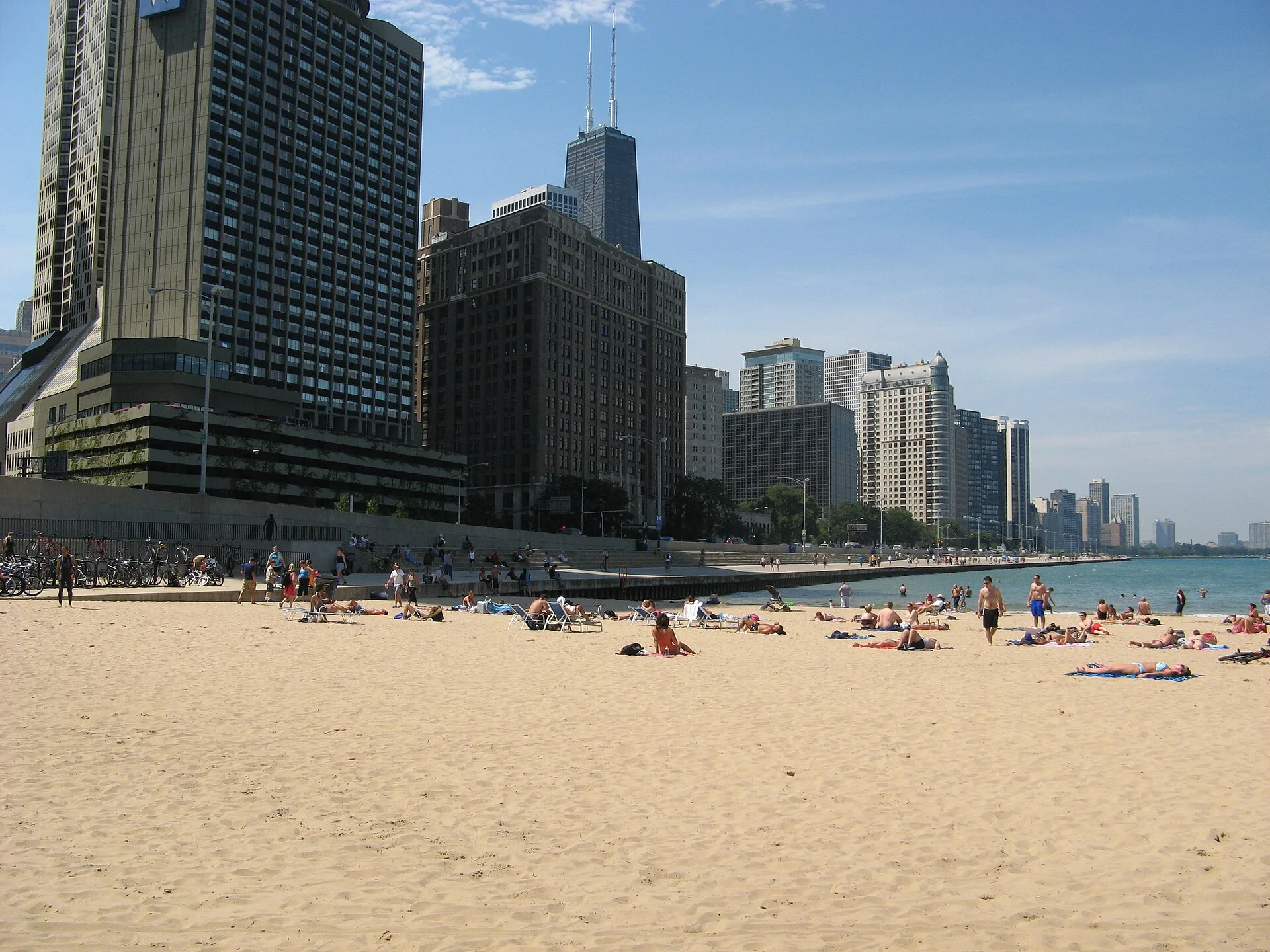 Faixa de areia de Ohio Street Beach com pessoas distantes em terra, edifícios altos de Chicago e Lago Michigan ao fundo.